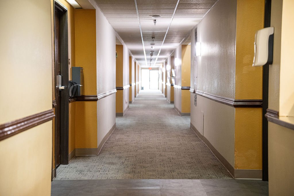 Hallway at Valley View Recovery Center with yellow and beige walls, carpeted floor, and ceiling lights.