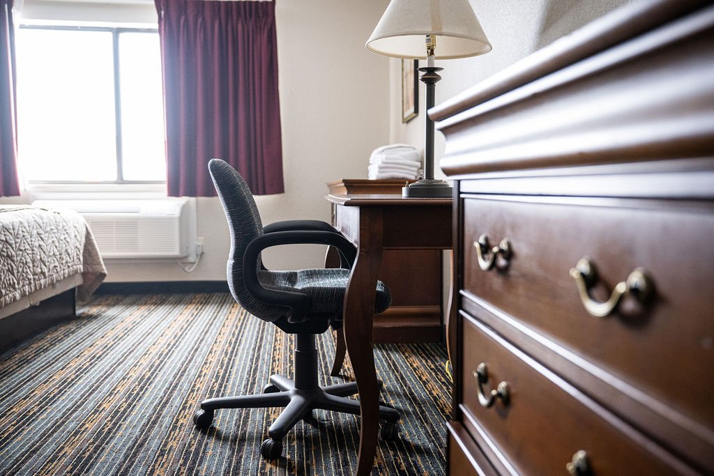 Room with a bed, window, desk, chair, dresser, and a table lamp.