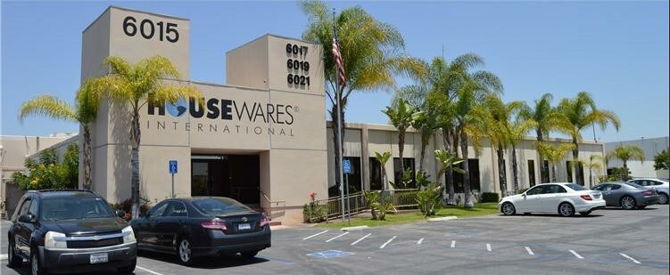 Exterior view of a commercial building with palm trees and parked cars, labeled 'Housewares International' with addresses '6015, 6017, 6019, 6021'.