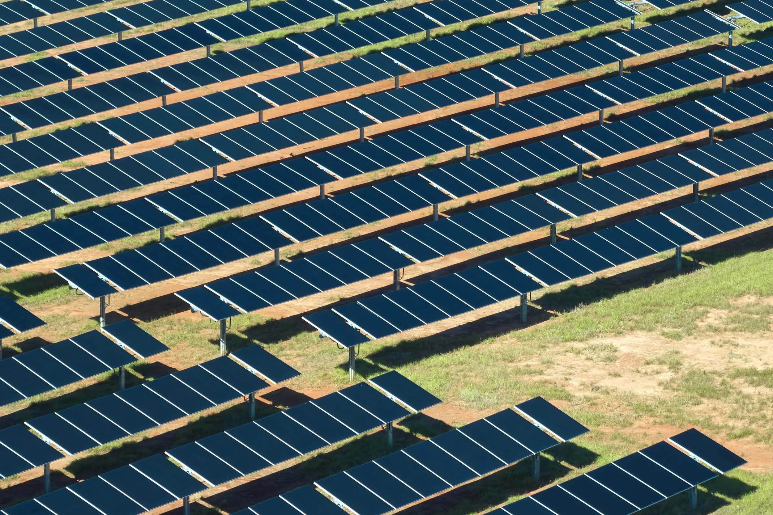 A large solar farm with rows of solar panels installed on metal frames on grassy land.