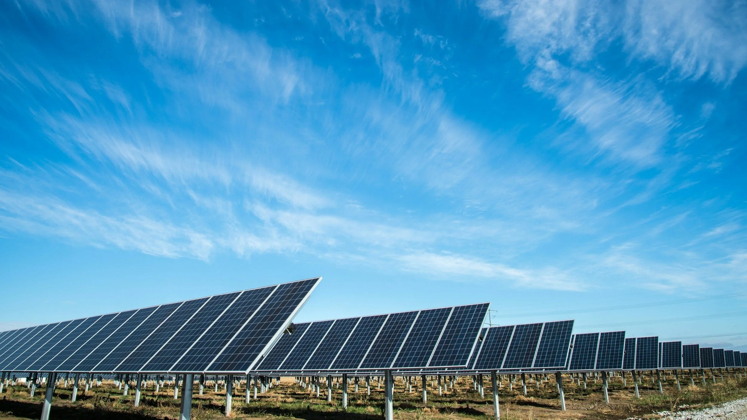 A field of solar panels under a blue sky with wispy clouds.