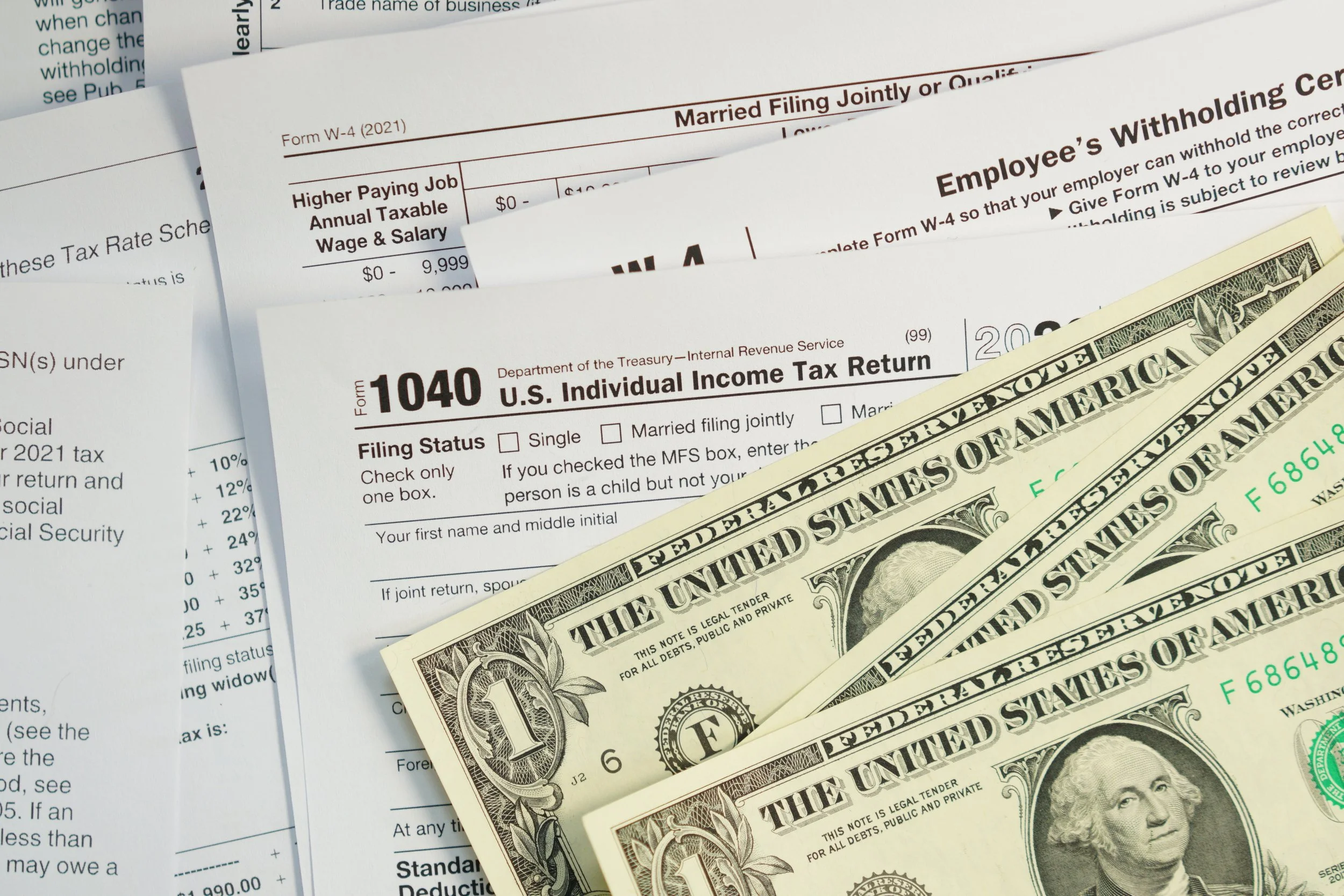 U.S. dollar bills placed on top of tax documents, including Form 1040 and employer withholding forms.