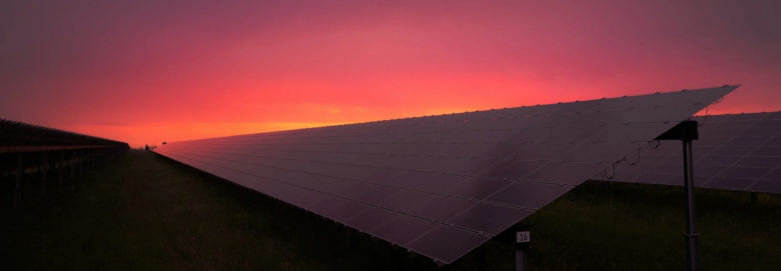 Solar panels on a field at sunset with a colorful pink and orange sky.