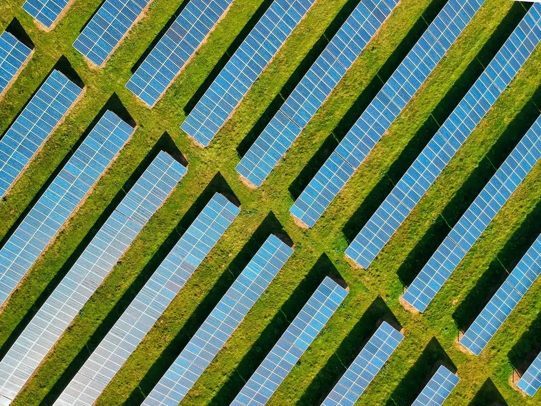 An aerial view of multiple solar panel arrays arranged in rows on a grassy field.
