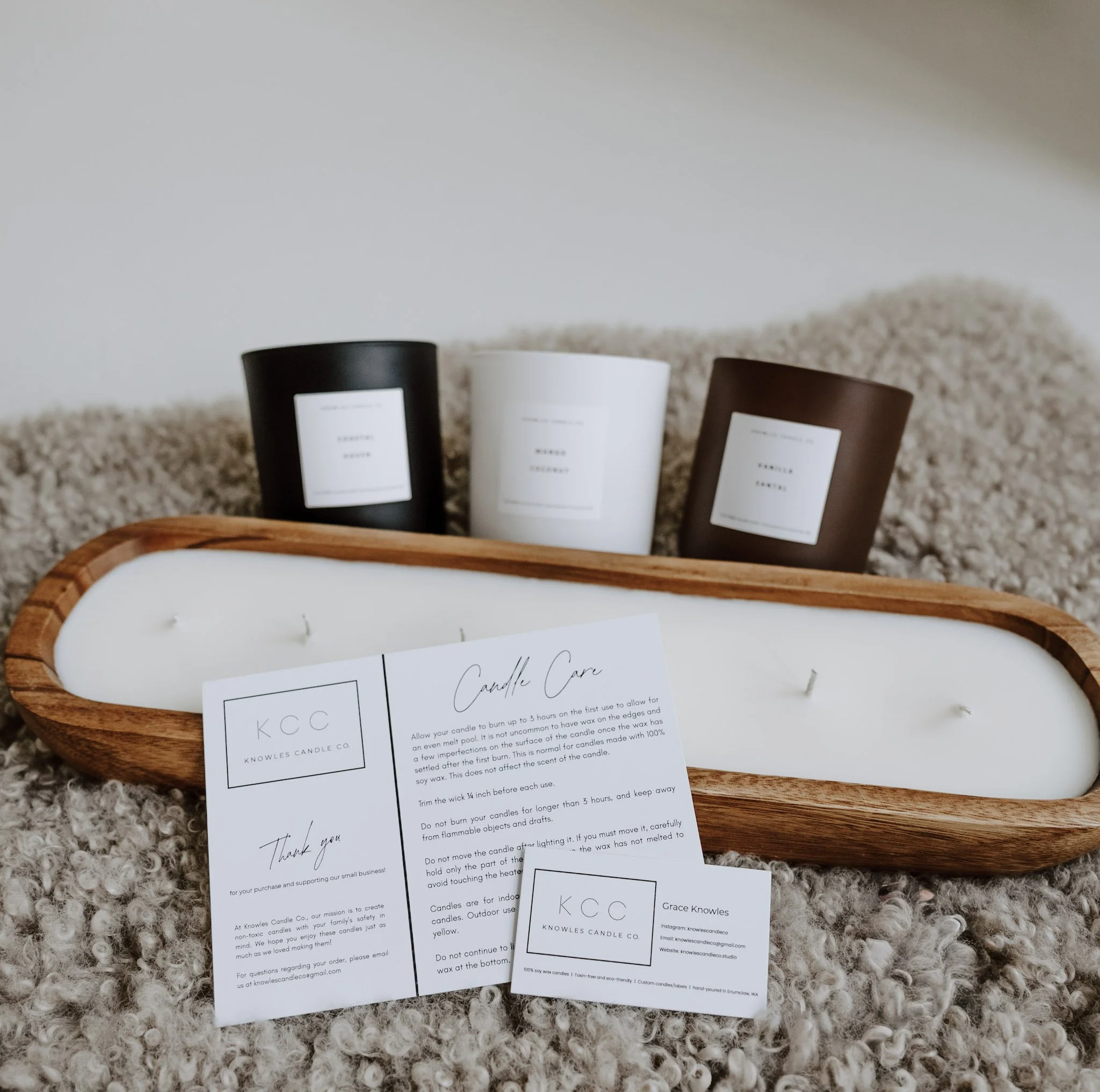 Wooden dough bowl candle with white wax and multiple wicks, displayed with Knowles Candle Co. candle care card, business card, and three jar candles in black, white, and brown vessels in the background