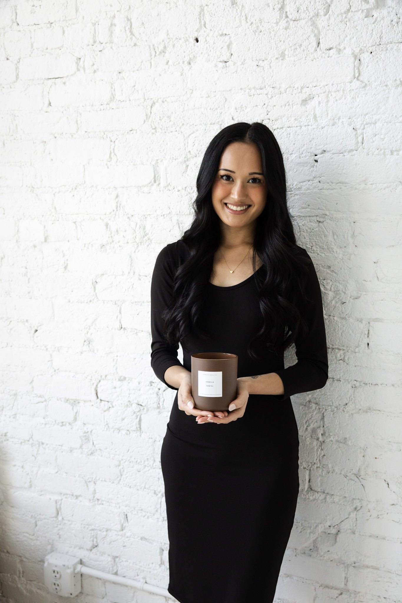 Candle owner holding a brown candle while standing in a bright, neutral setting