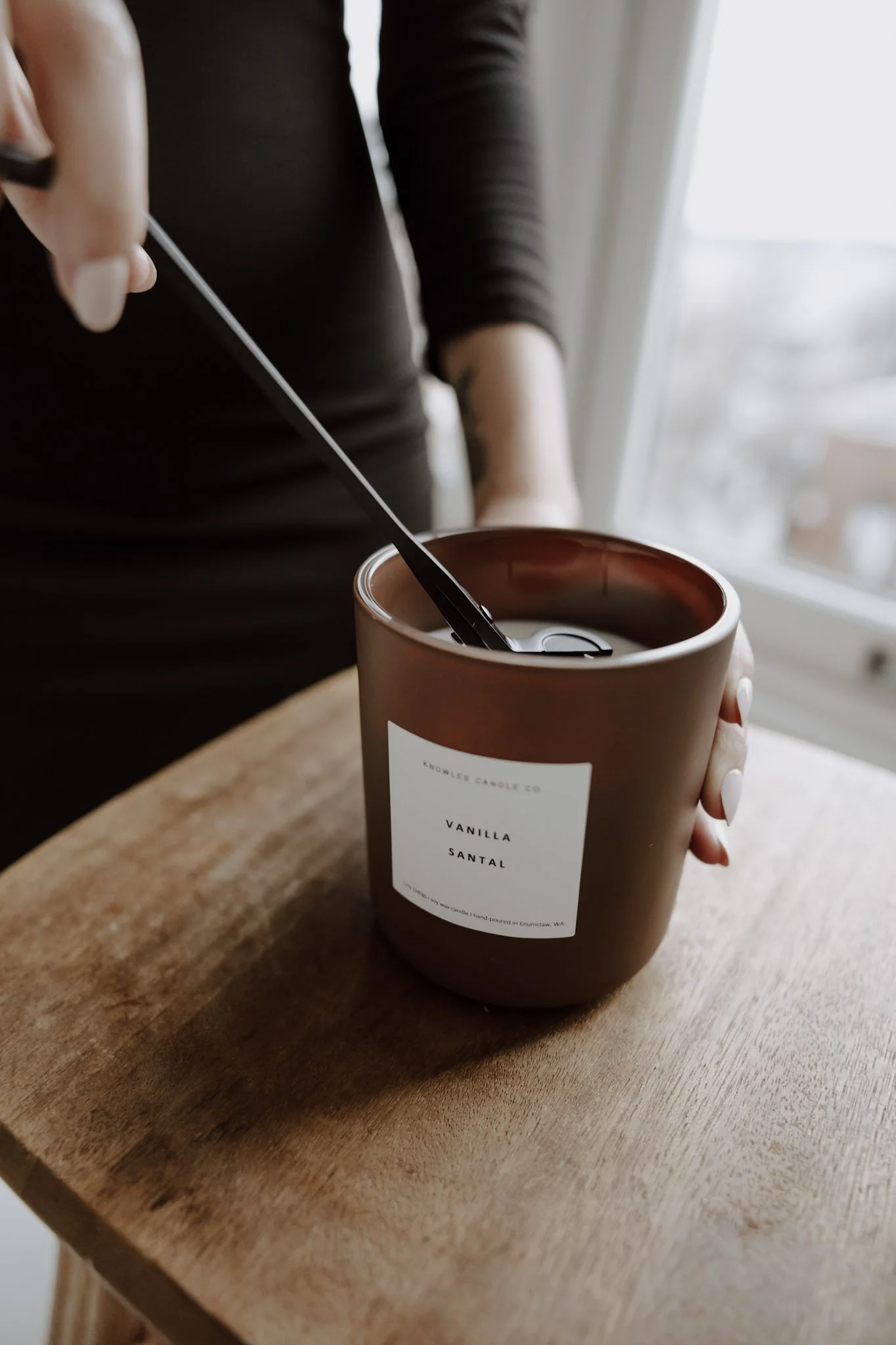 Candle maker trimming the wick of a brown, hand-poured candle