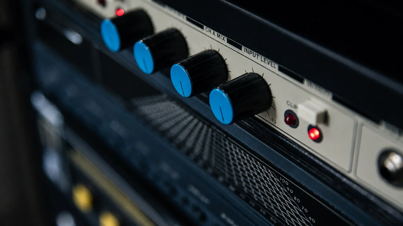 Close-up of audio equipment control panel with black knobs featuring blue tops, labels for input levels, and indicator lights.