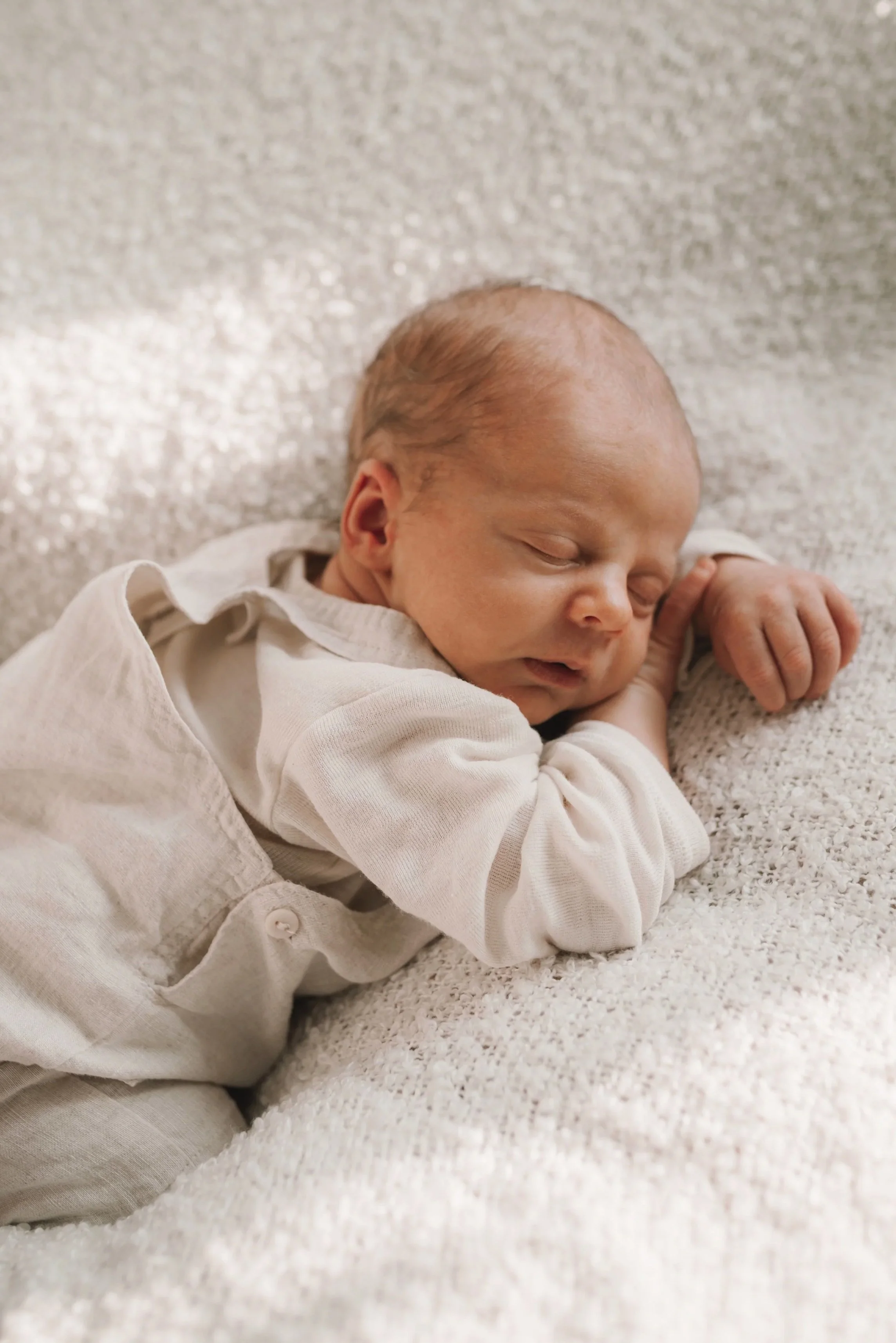 Ein neugeborenes Baby liegt schlafend auf einem cremefarbenen, texturierten Stoff.