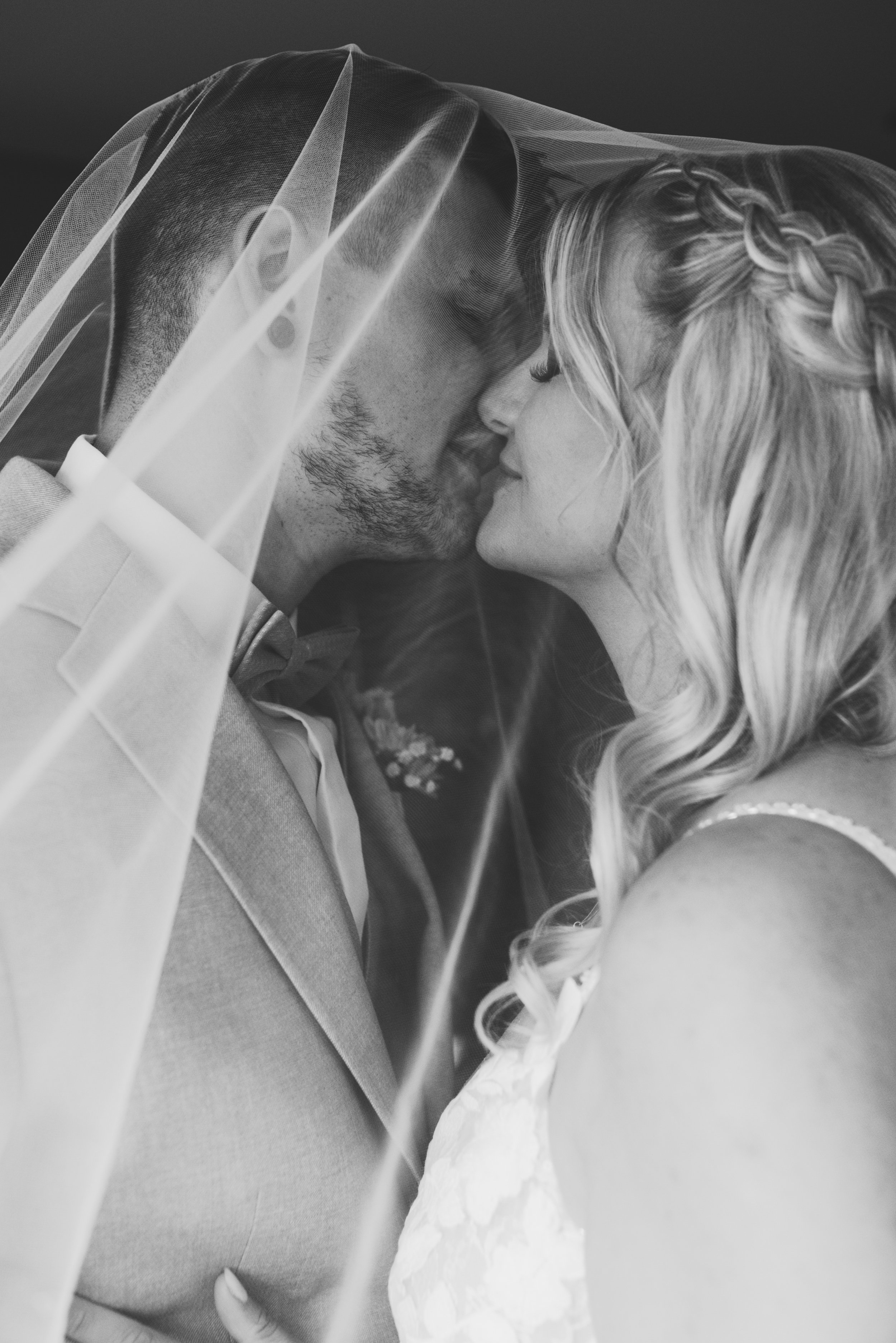 Ein Brautpaar küsst sich unter einem Schleier bei ihrer Hochzeit, schwarz-weiß Fotografie.