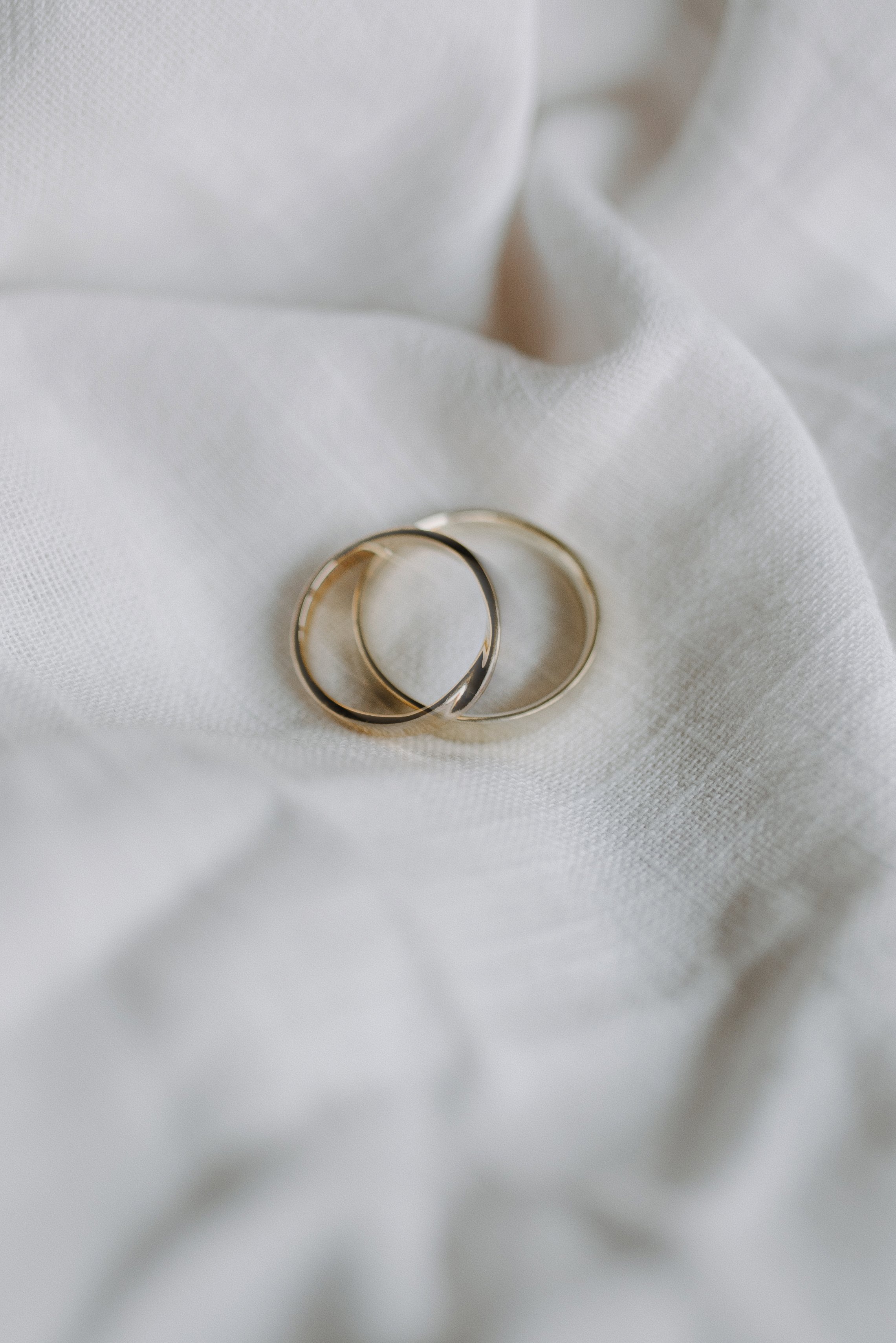 Zwei goldene Eheringe liegen auf weißem Stoff mit Falten