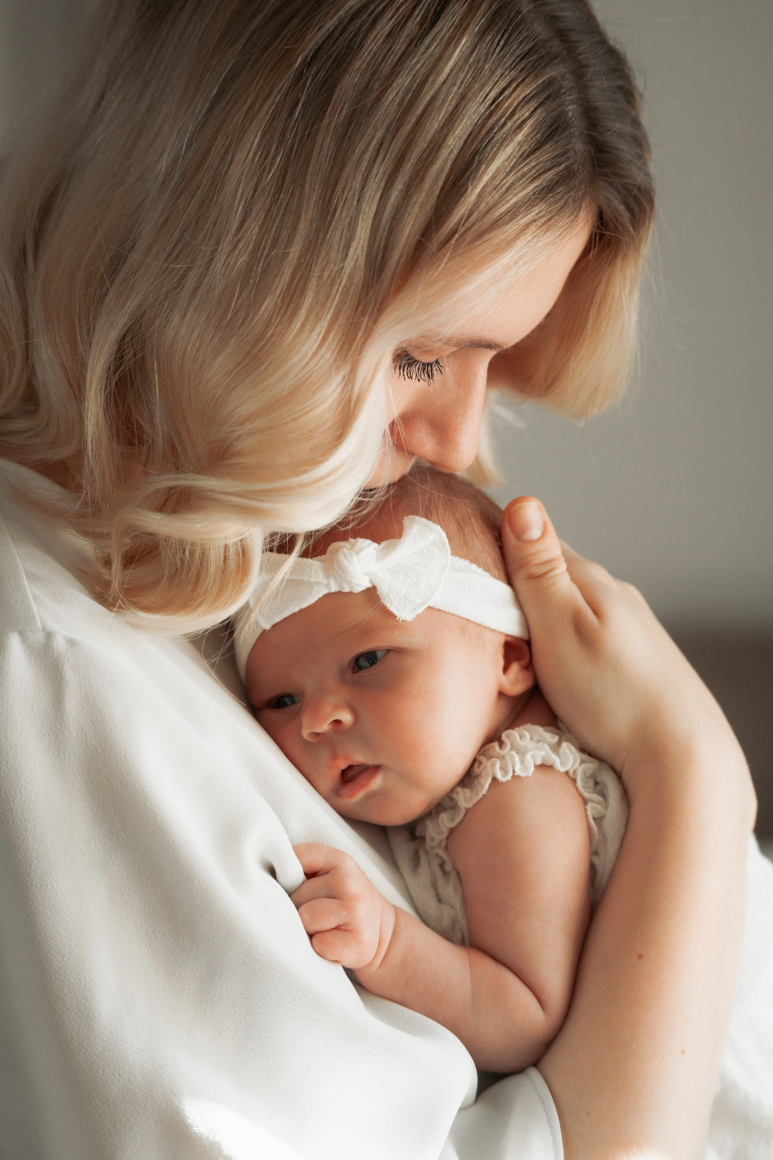 Eine Frau hält ein Neugeborenes in den Armen, das einen weißen Haarschmuck trägt.