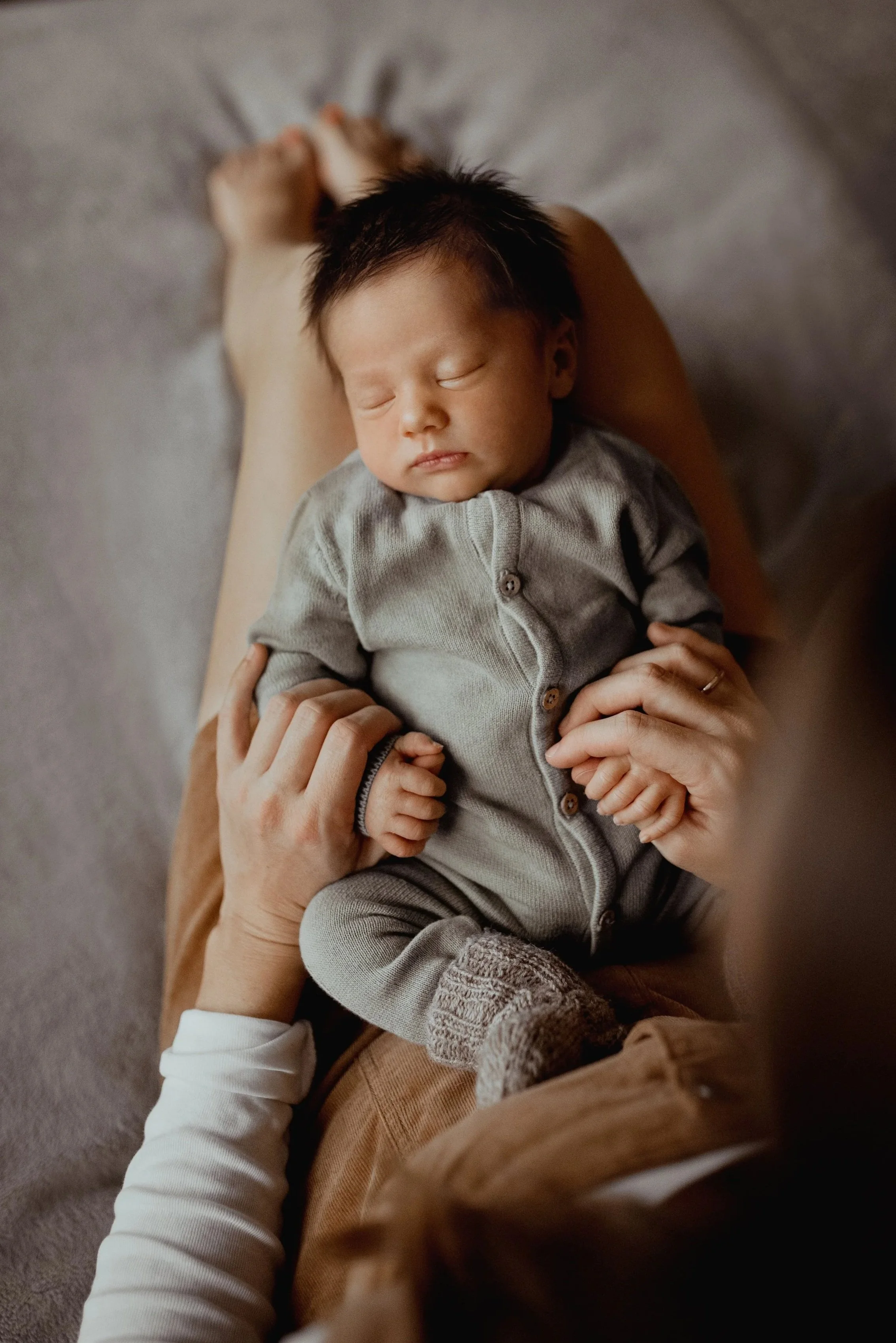Ein schlafender neugeborener Junge, der auf den Beinen einer Person liegt und gehalten wird.