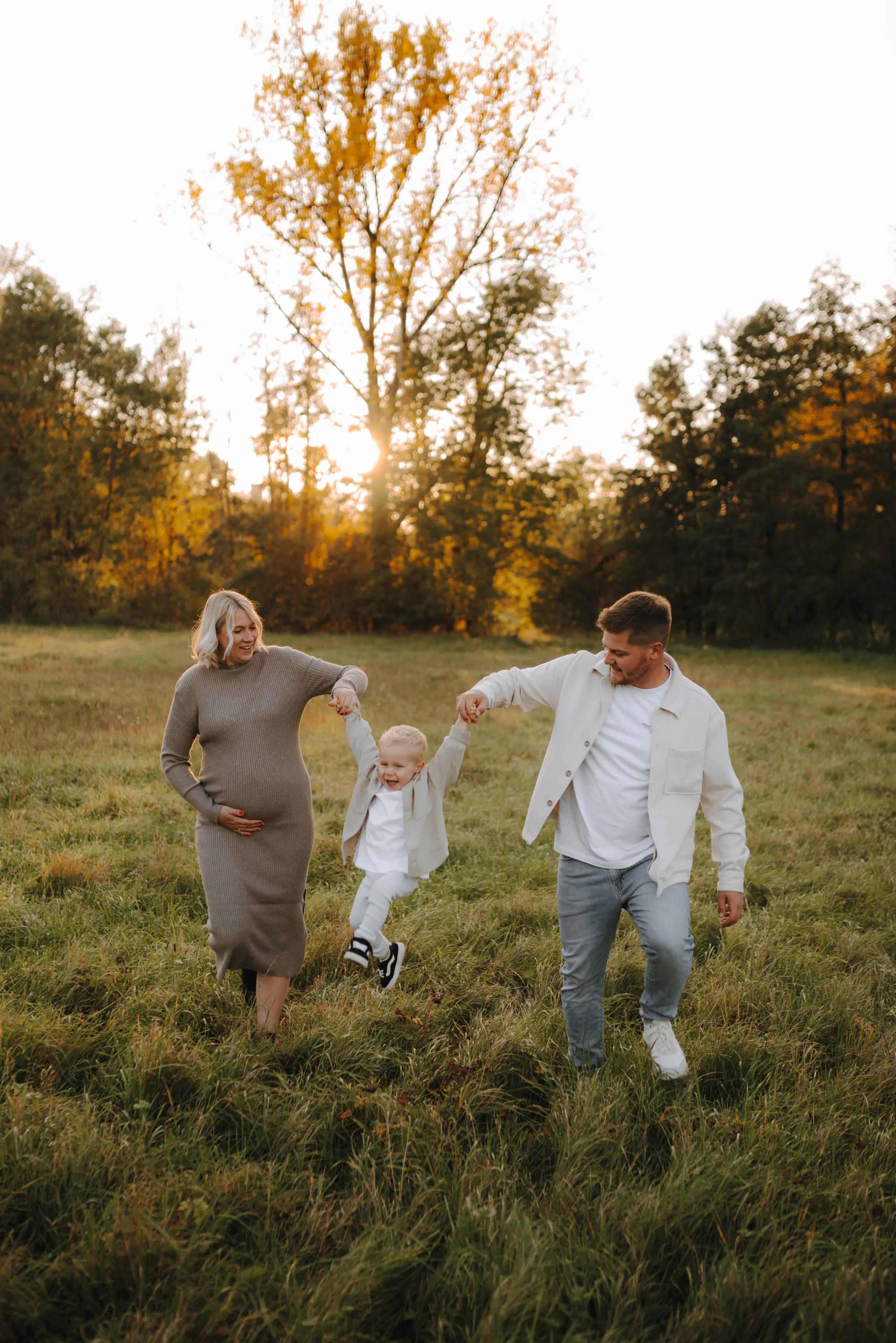 Familie mit Baby beim Spaziergang im Herbstwald, Sonnenuntergang, natürliche Umgebung, Glückliche Stimmung.