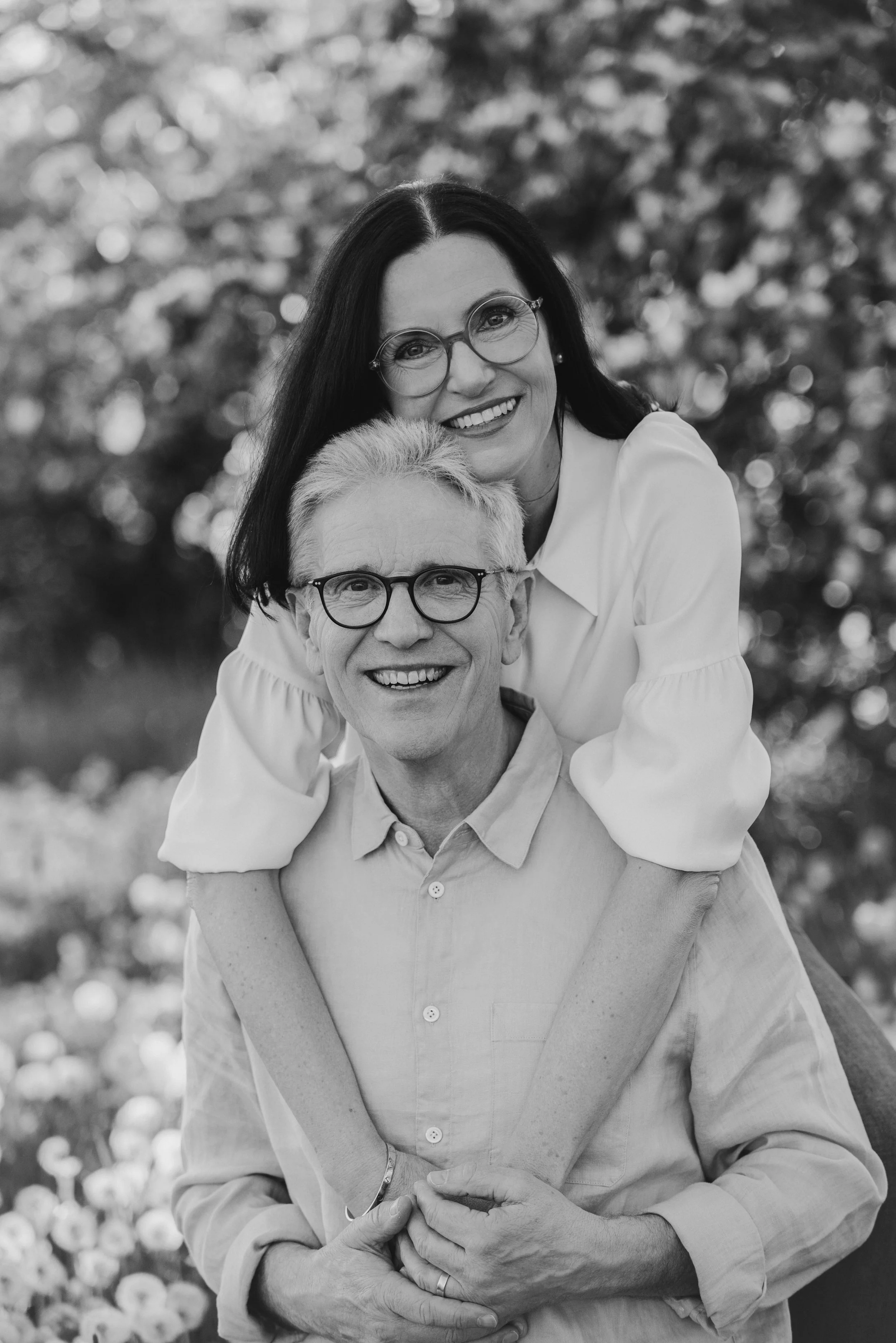 Ein älteres Paar, beide mit Brillen, lächelnd in einem Garten, schwarz-weiß