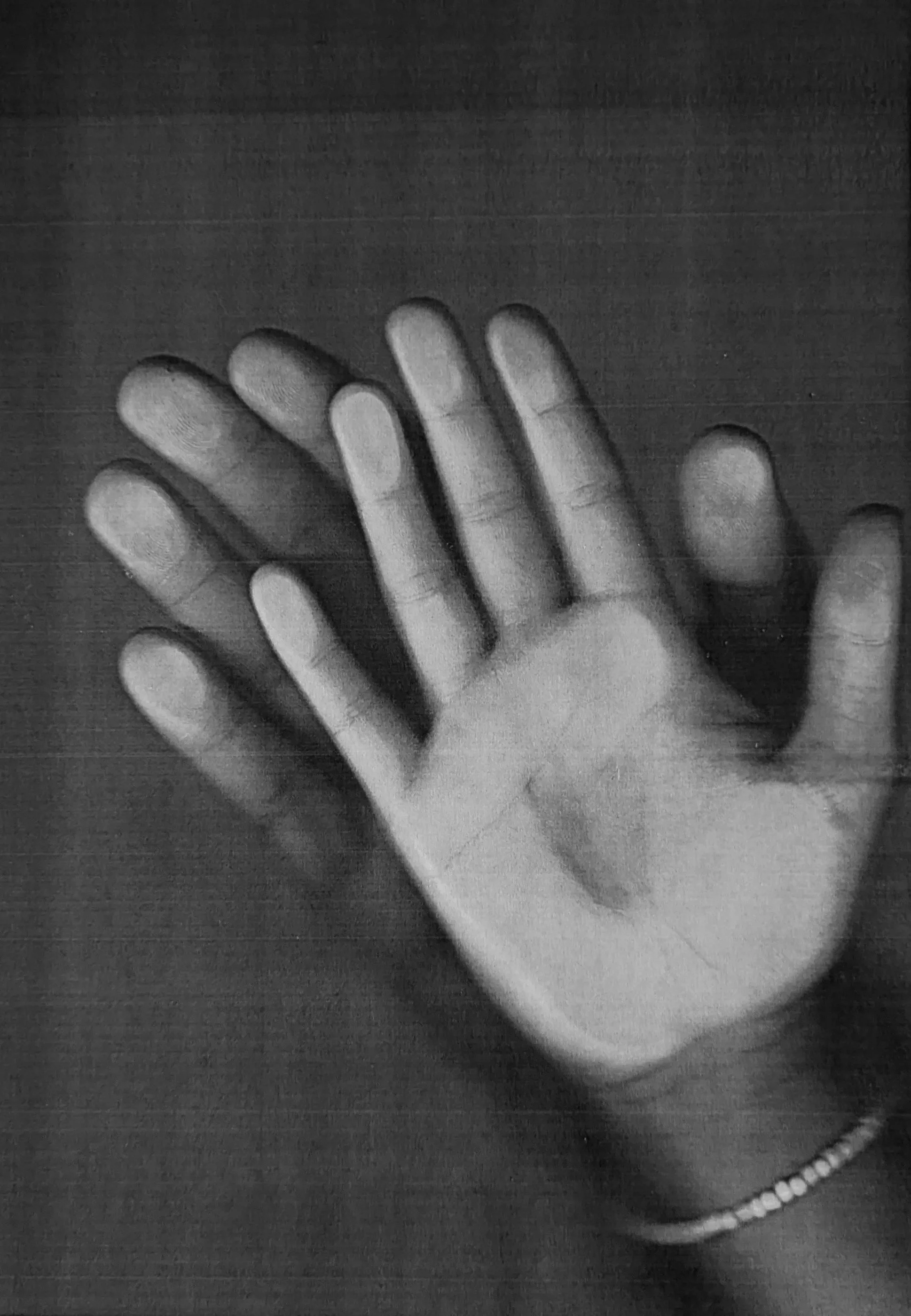 Schwarz-weiß-Foto einer Hand mit gespreizten Fingern auf einer dunklen Oberfläche, mit einem Armband am Handgelenk.