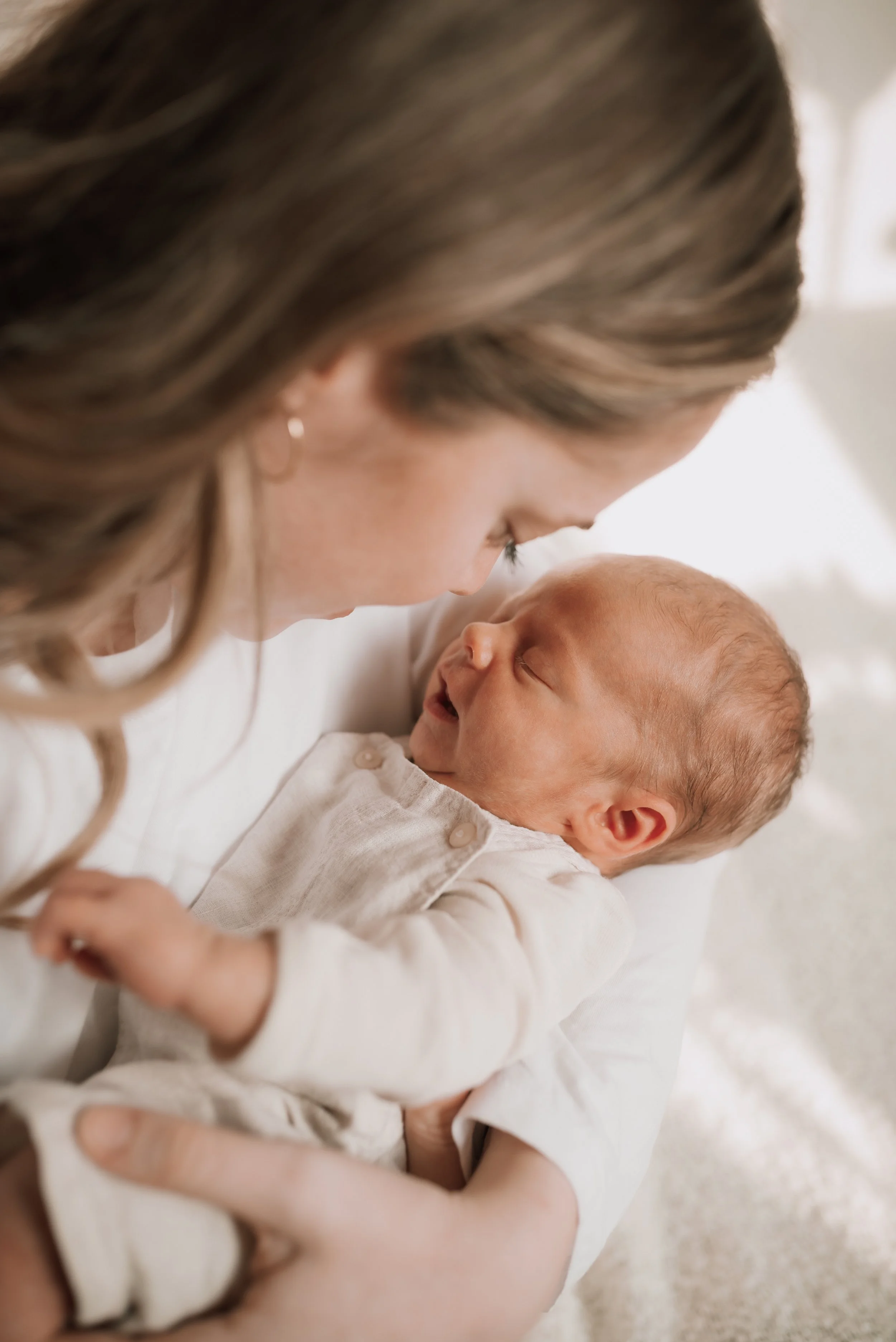 Eine Frau hält ein schlafendes Baby in ihren Armen, sie schauen sich liebevoll an.