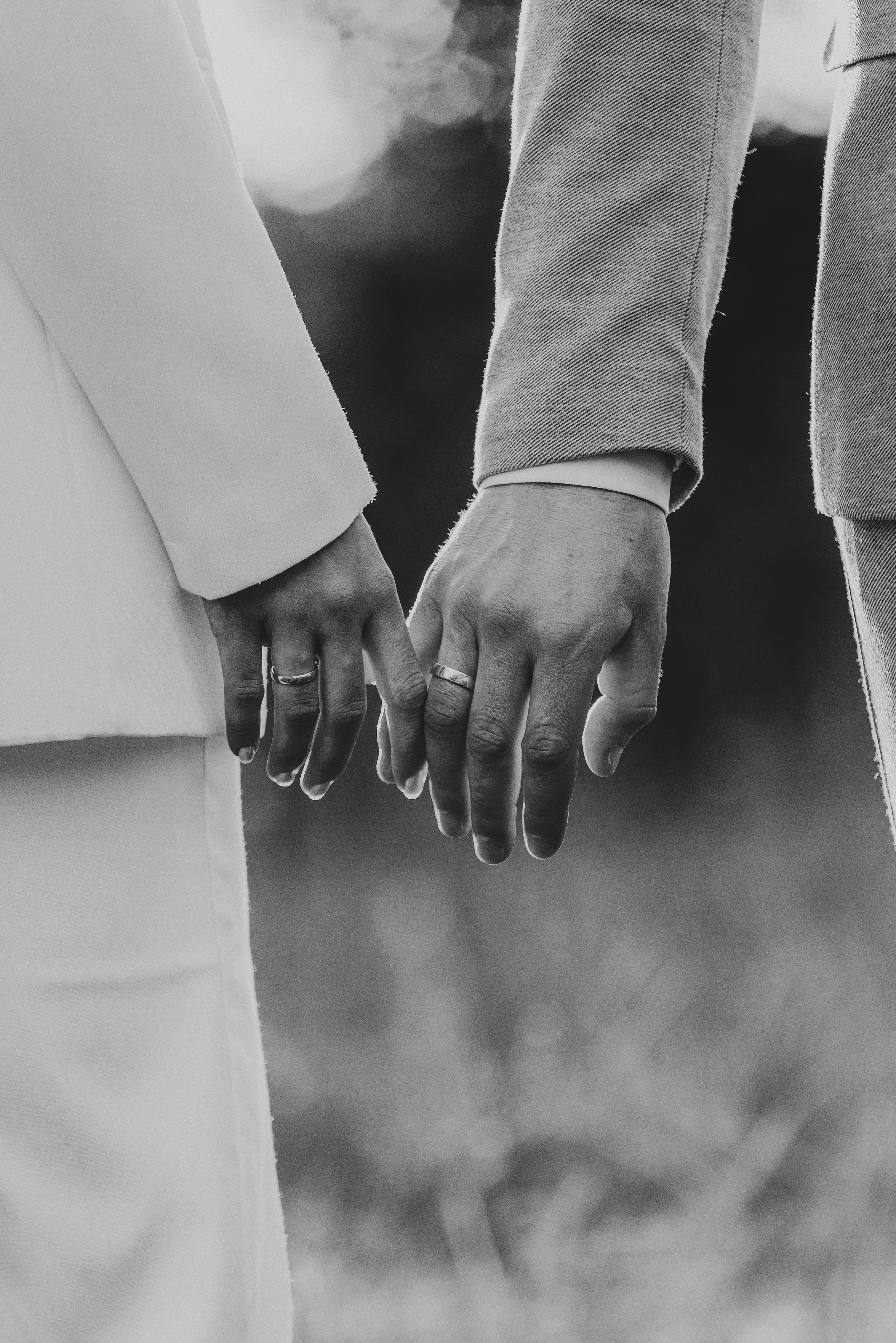 Zwei Hände, die sich halten, mit Hochzeitsringen, in Schwarz-Weiß-Fotografie.