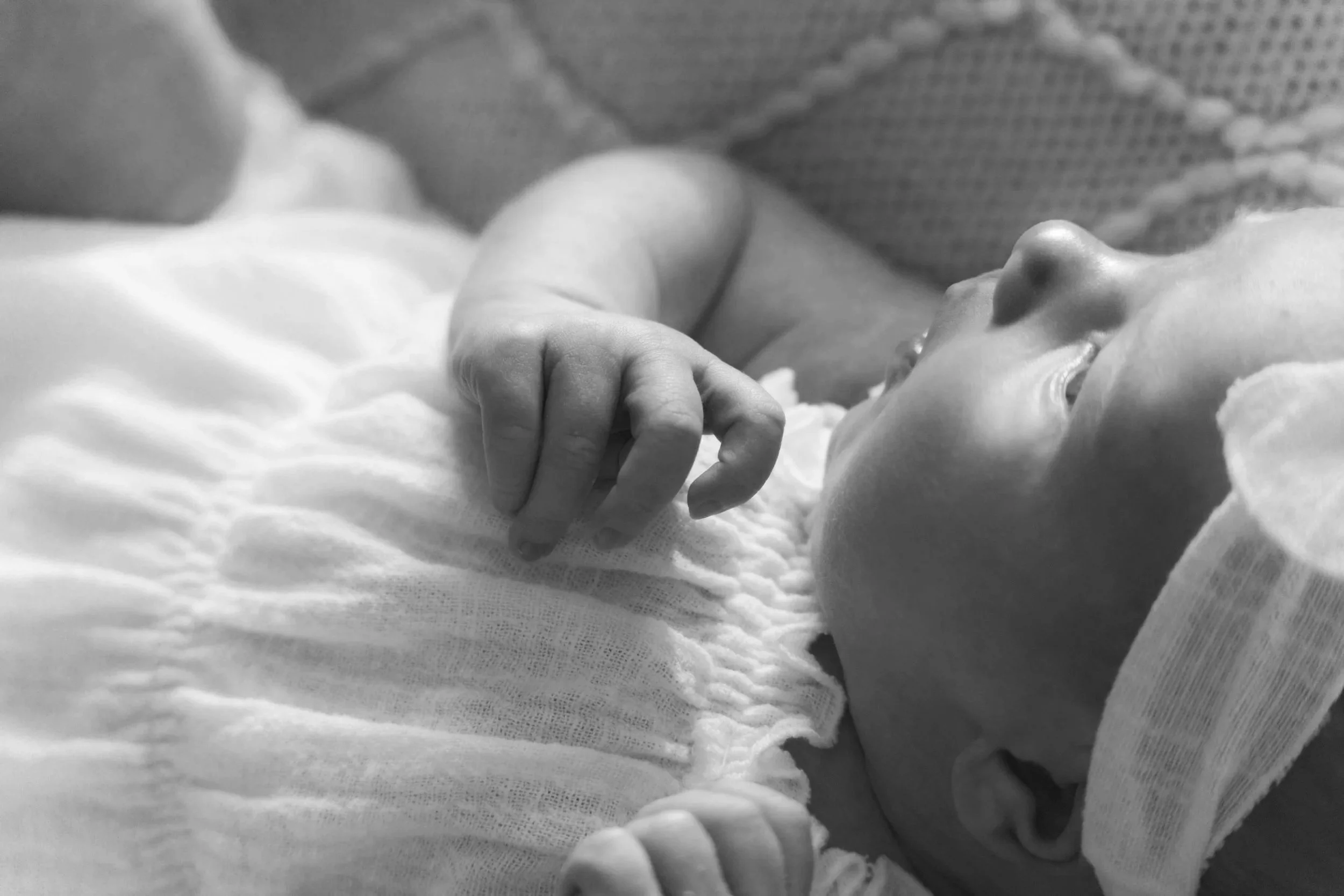 Ein neugeborenes Baby liegt auf einem weichen Bett und schaut nach oben, mit einer Hand in die Luft. Das Baby trägt einen Kopfhörer auf dem Kopf.