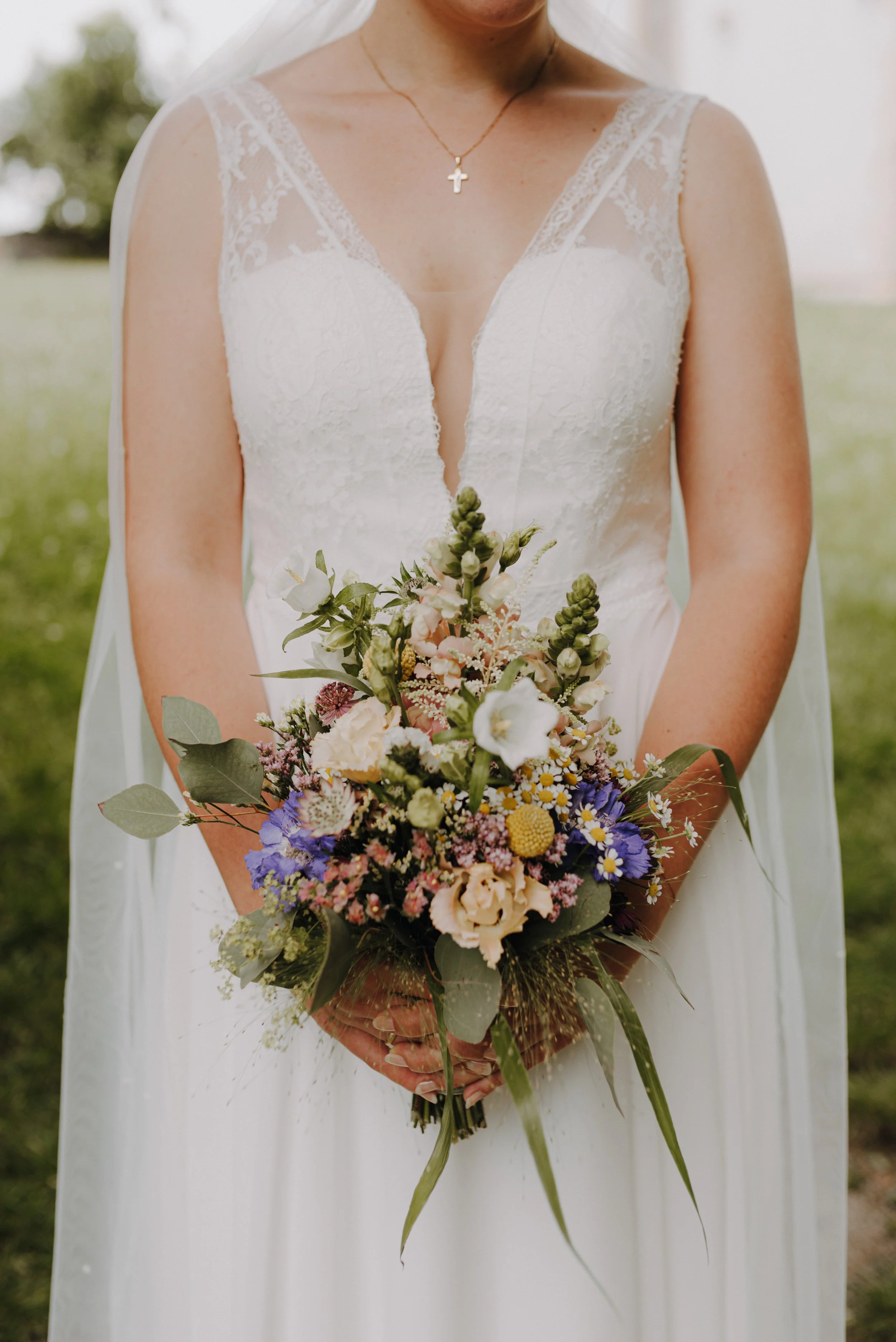 Nahaufnahme einer Braut in weißem Kleid mit Blumenstrauß vor grünem Hintergrund.