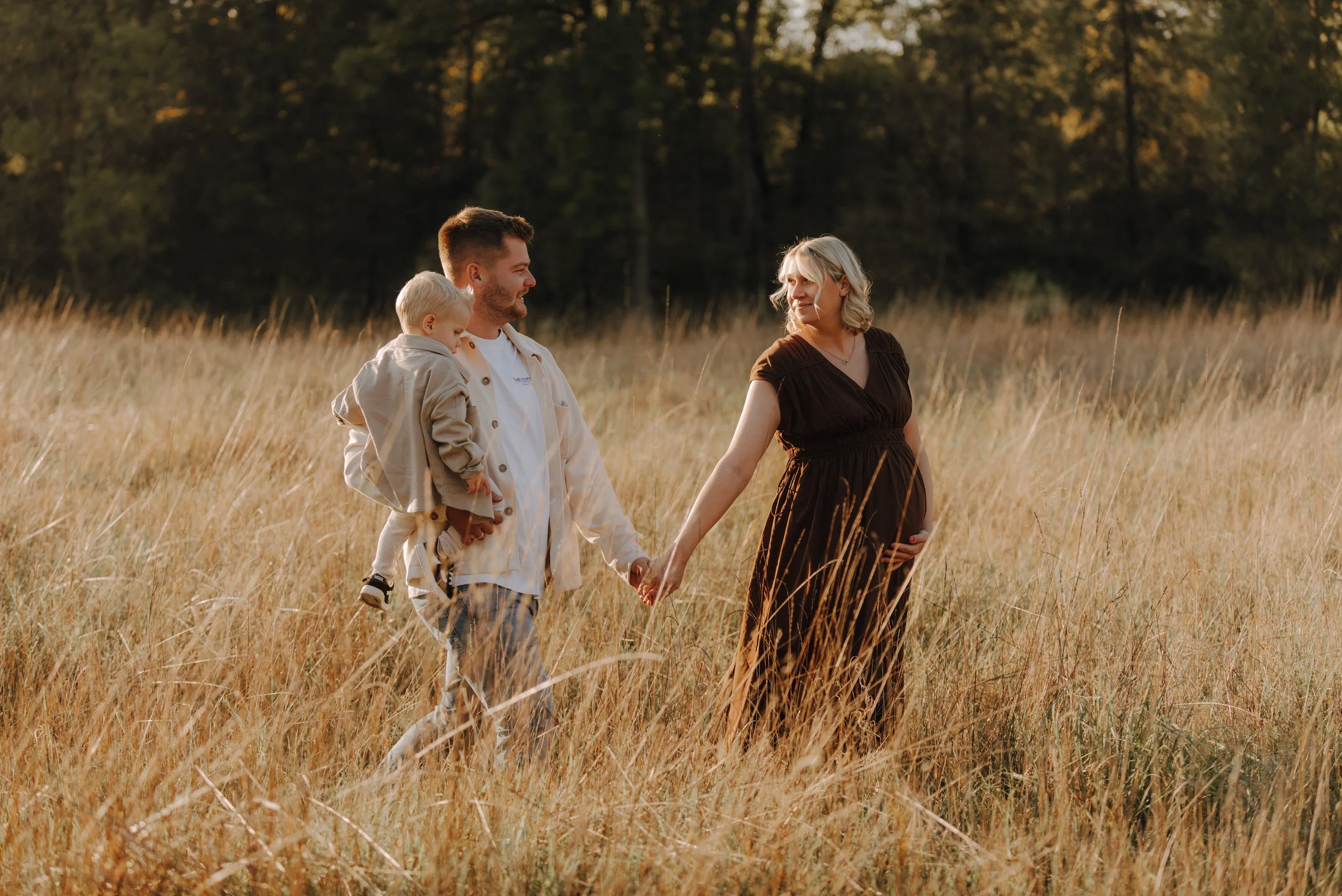 Ein glückliches Paar mit einem kleinen Kind in einem goldenen Feld bei Sonnenuntergang, Hände haltend.