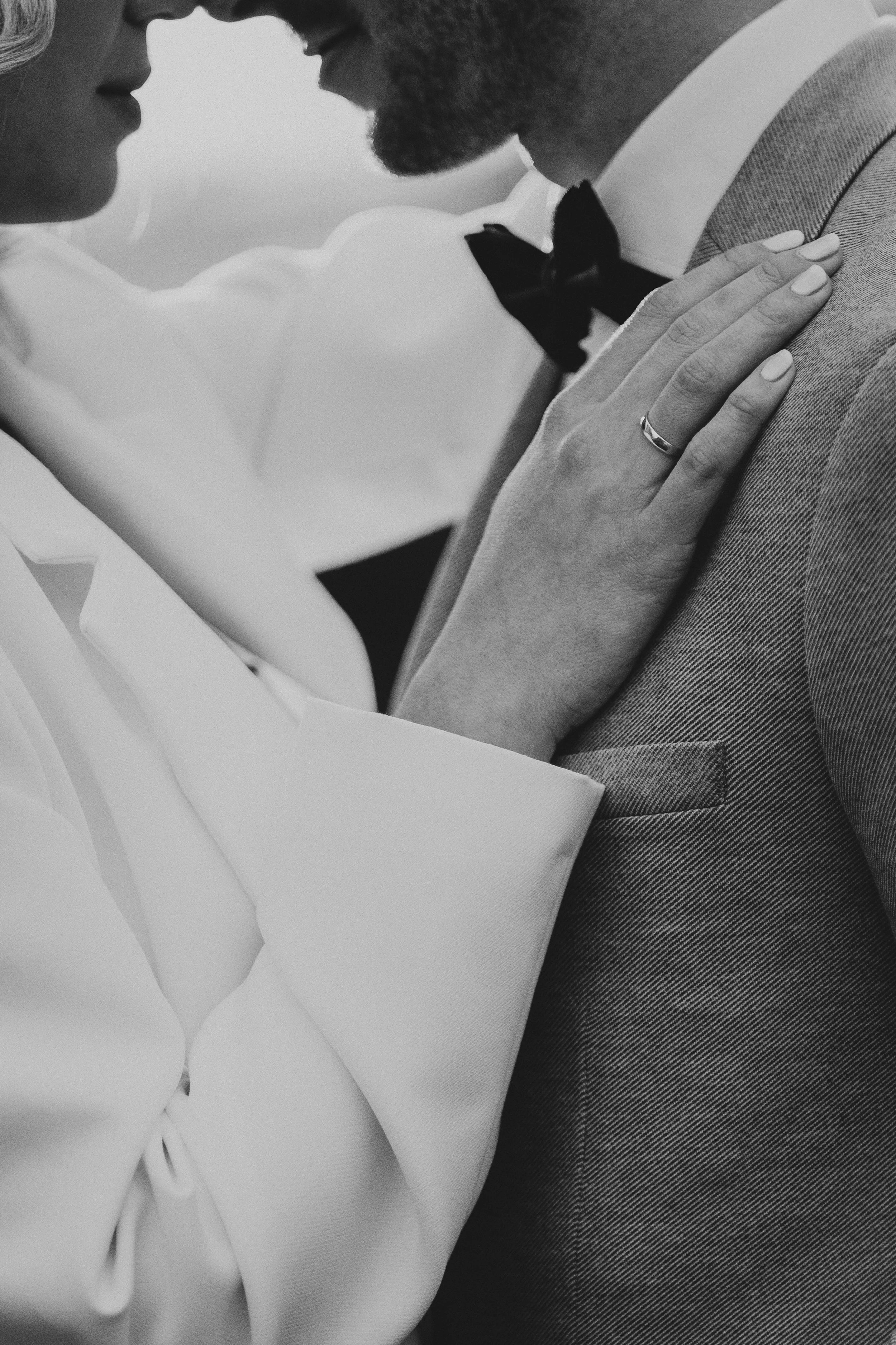 Nahaufnahme eines Paares in formeller Kleidung, das sich nahe kommt, mit Fokus auf ihre Hände und Hüften, schwarz-weiß Fotografie.