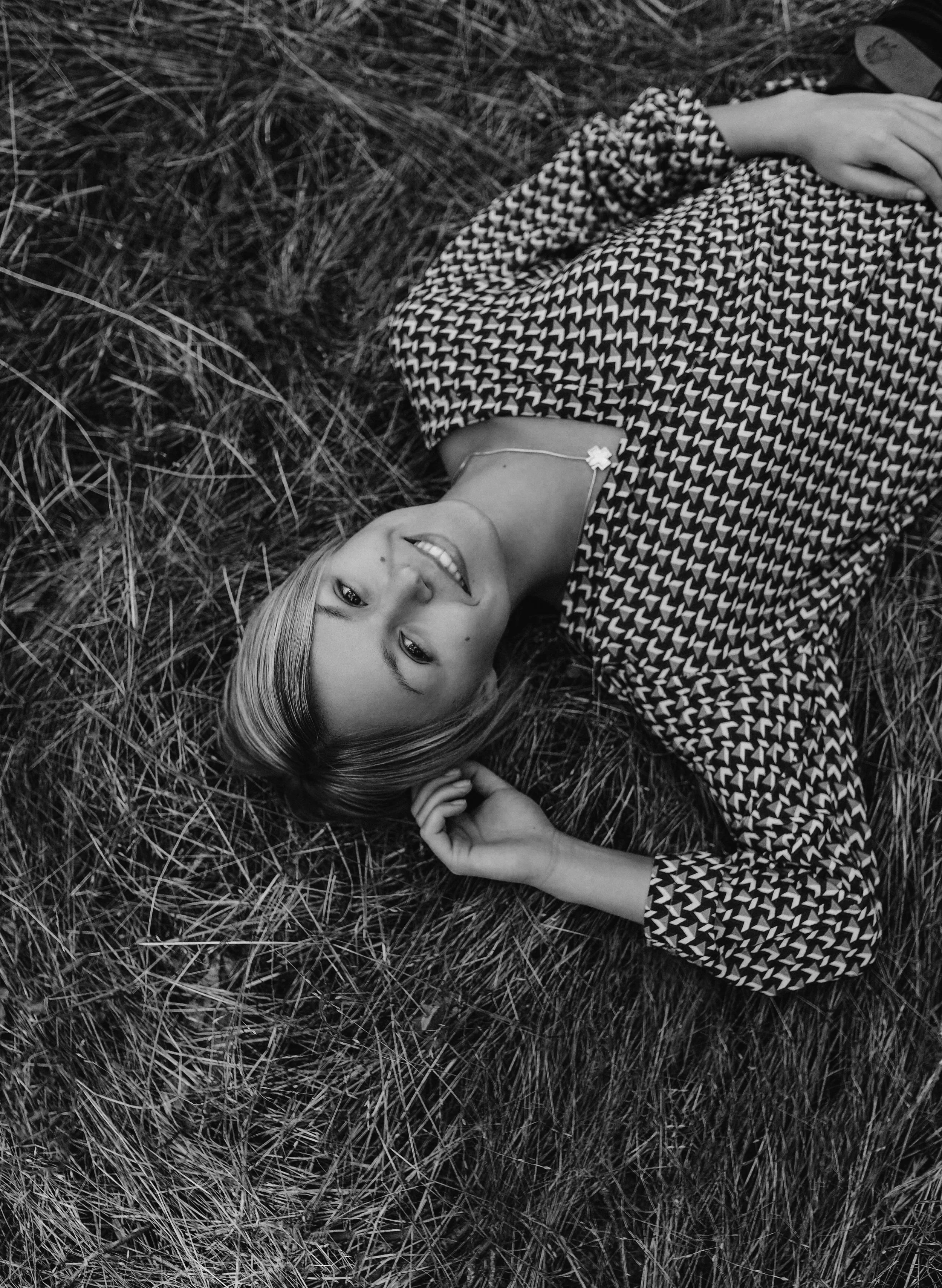 Ein Mädchen liegt auf den Boden, umgeben von trockenem Gras, und lächelt in die Kamera.