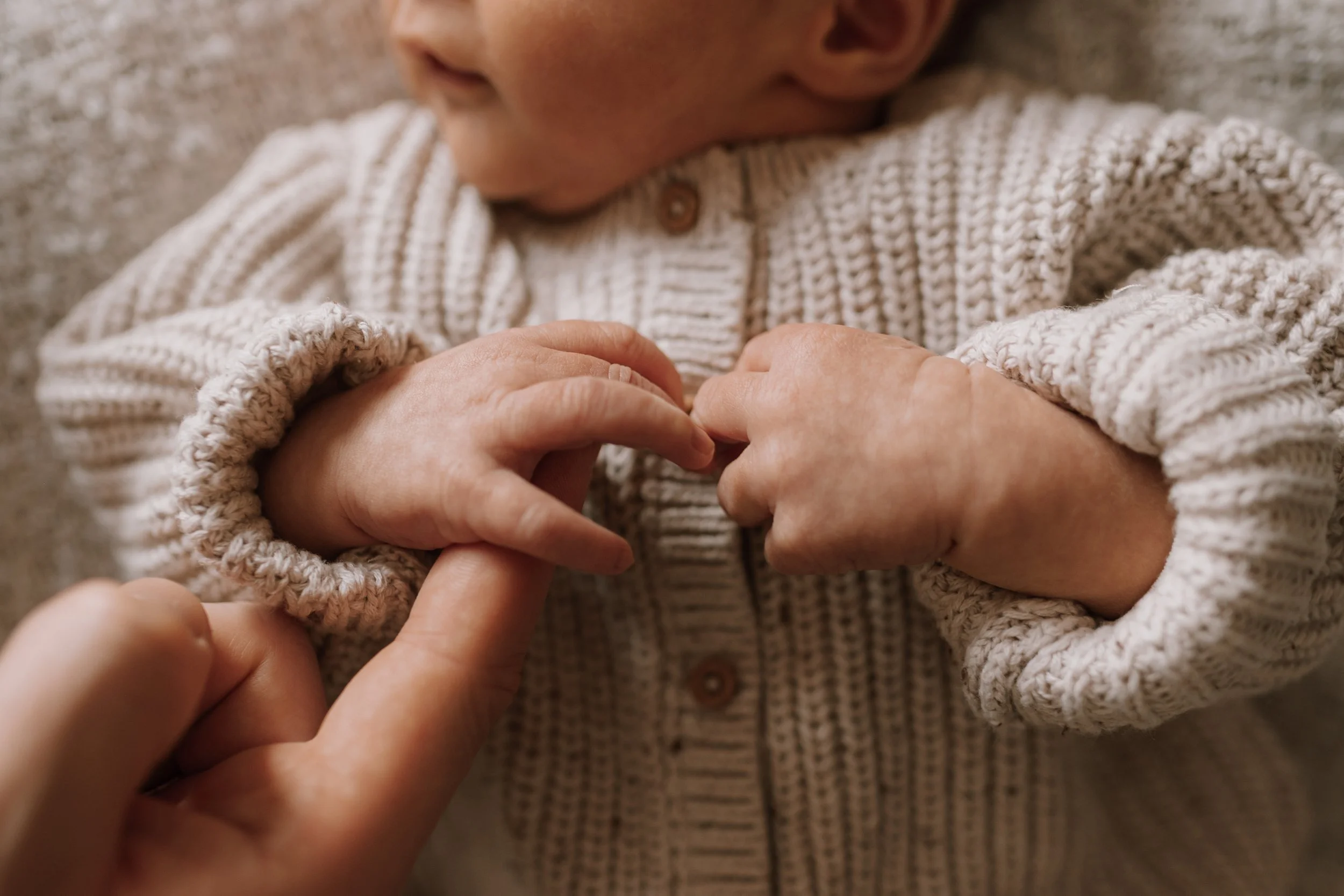 Nahaufnahme von einem Kind in einem wollenen Strickpullover, das seine kleinen Hände hält.