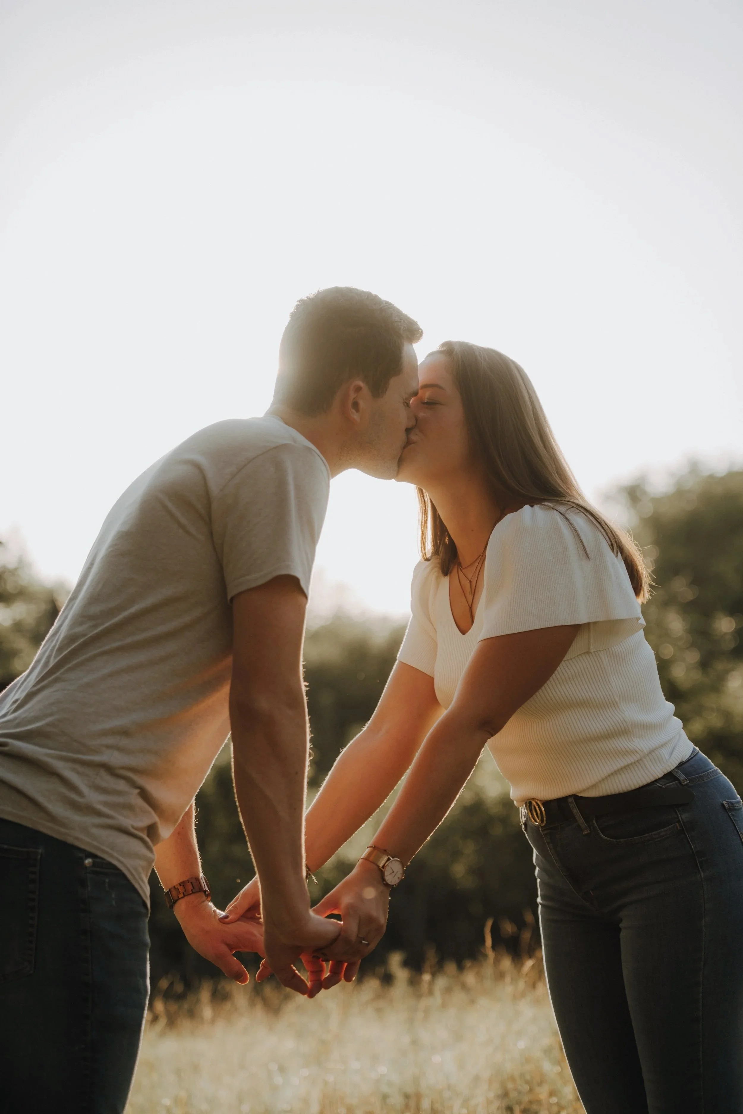 Ein Paar küsst sich in einem Feld bei Sonnenuntergang, hält Händchen und umarmt sich.