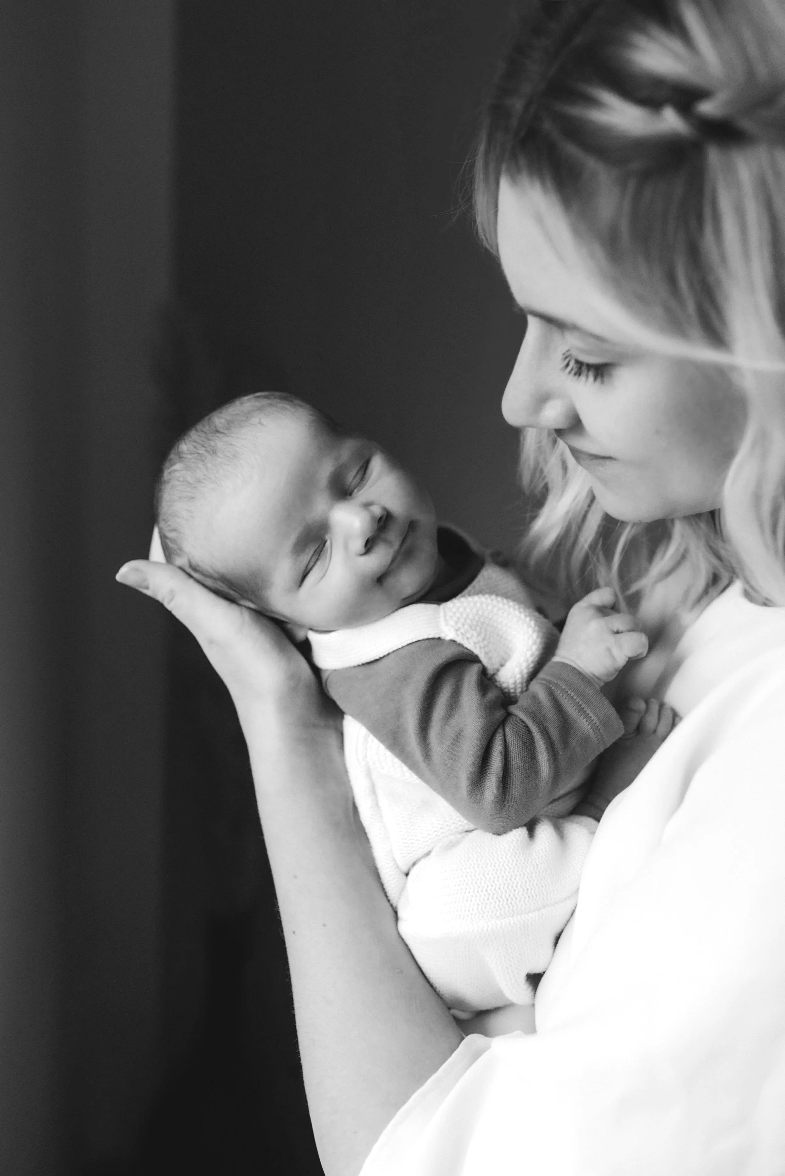 Eine Frau hält einen schlafenden Säugling liebevoll im Arm. Das Bild ist schwarz-weiß.