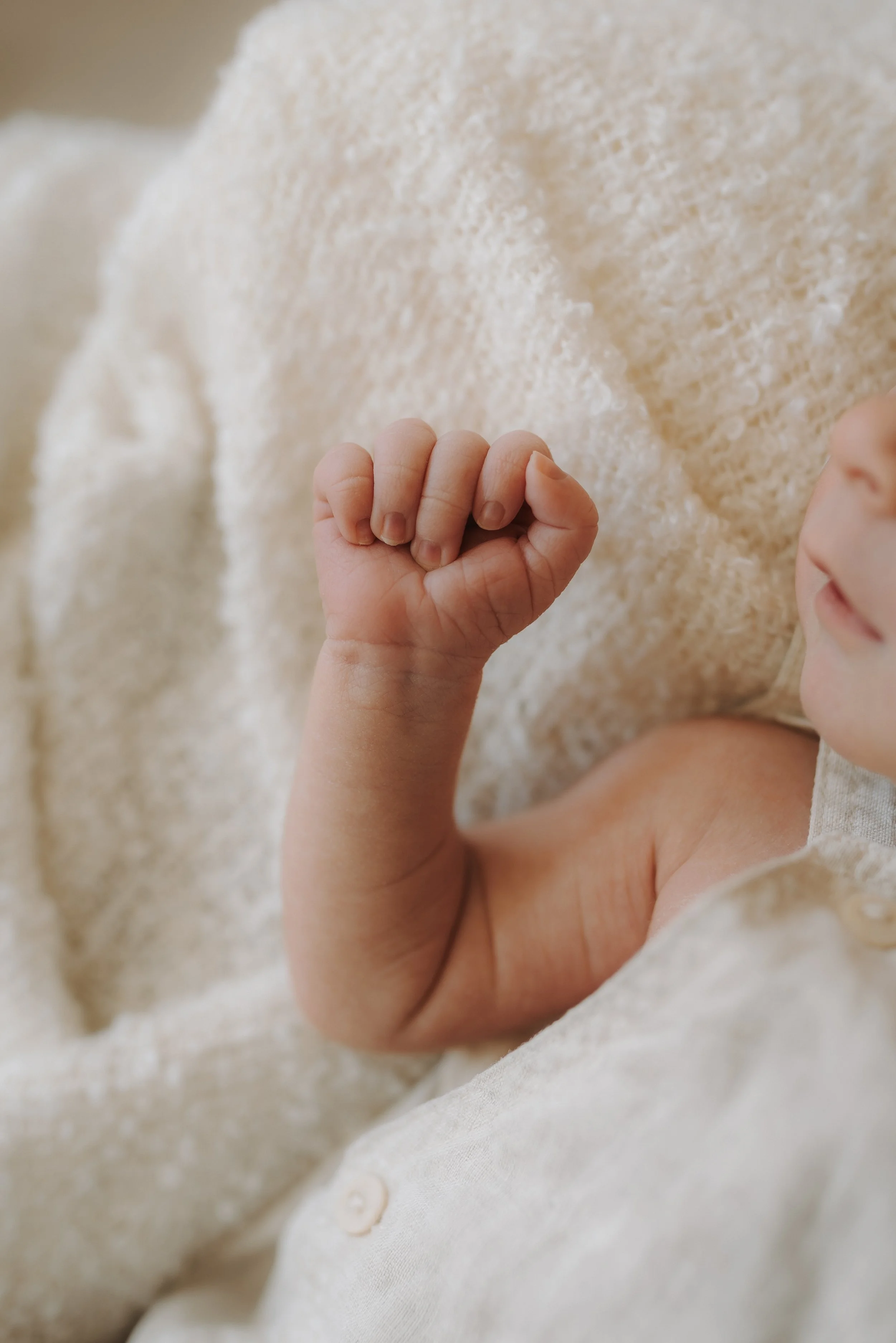 Nahaufnahme eines Erwachsenen, der eine Hand auf den Bauch eines Babys legt, das in einem Grau- und Grünton-Overall eingekleidet ist. Das Bild zeigt eine liebevolle Berührung zwischen zwei Personen.