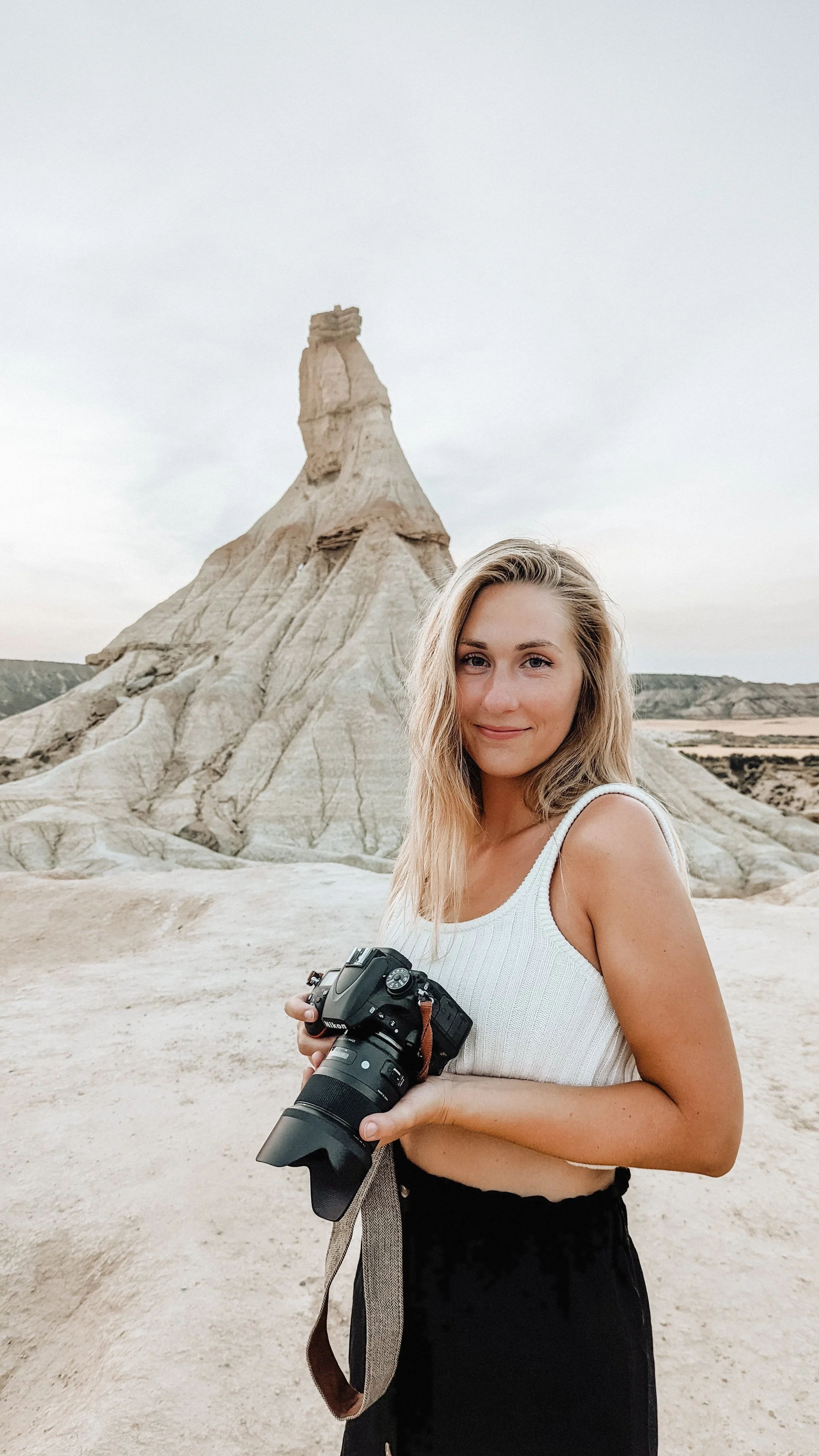Junge Frau mit Kamera in der Hand vor einer felsigen Landschaft und einer markanten Felsformation