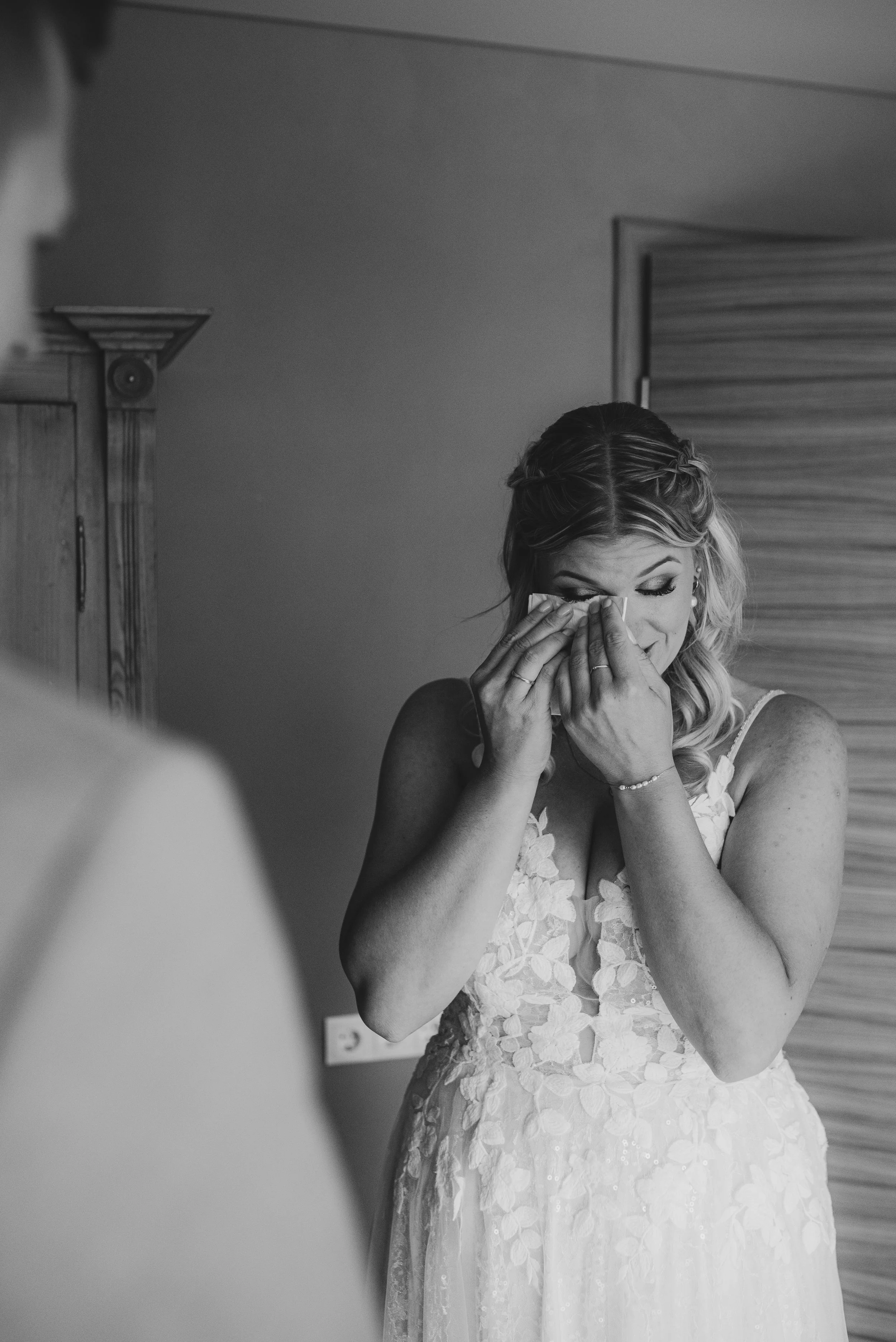 Eine Frau in einem Brautkleid weint und hält ein Taschentuch vor ihr Gesicht, während sie emotional ist.