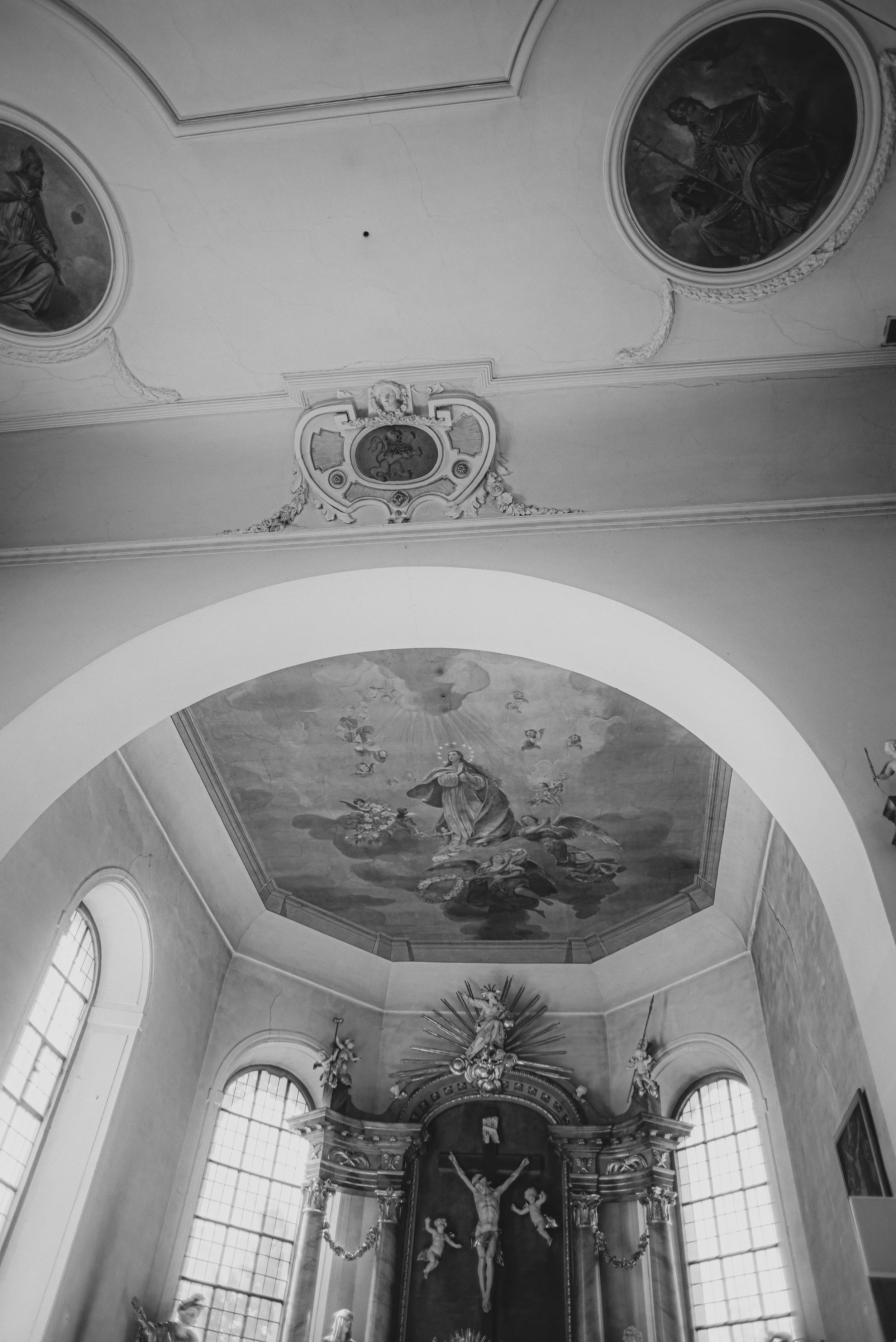 Innenraum einer Kirche mit gotischem Altar, bemalten Decken und hohen Fenstern, schwarz-weiß aufgenommen.