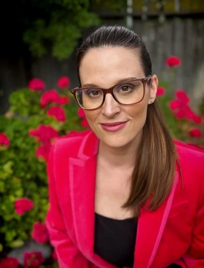 psychologist andrea hindes is wearing a hot pink blazer and is sitting in front of a blooming bush