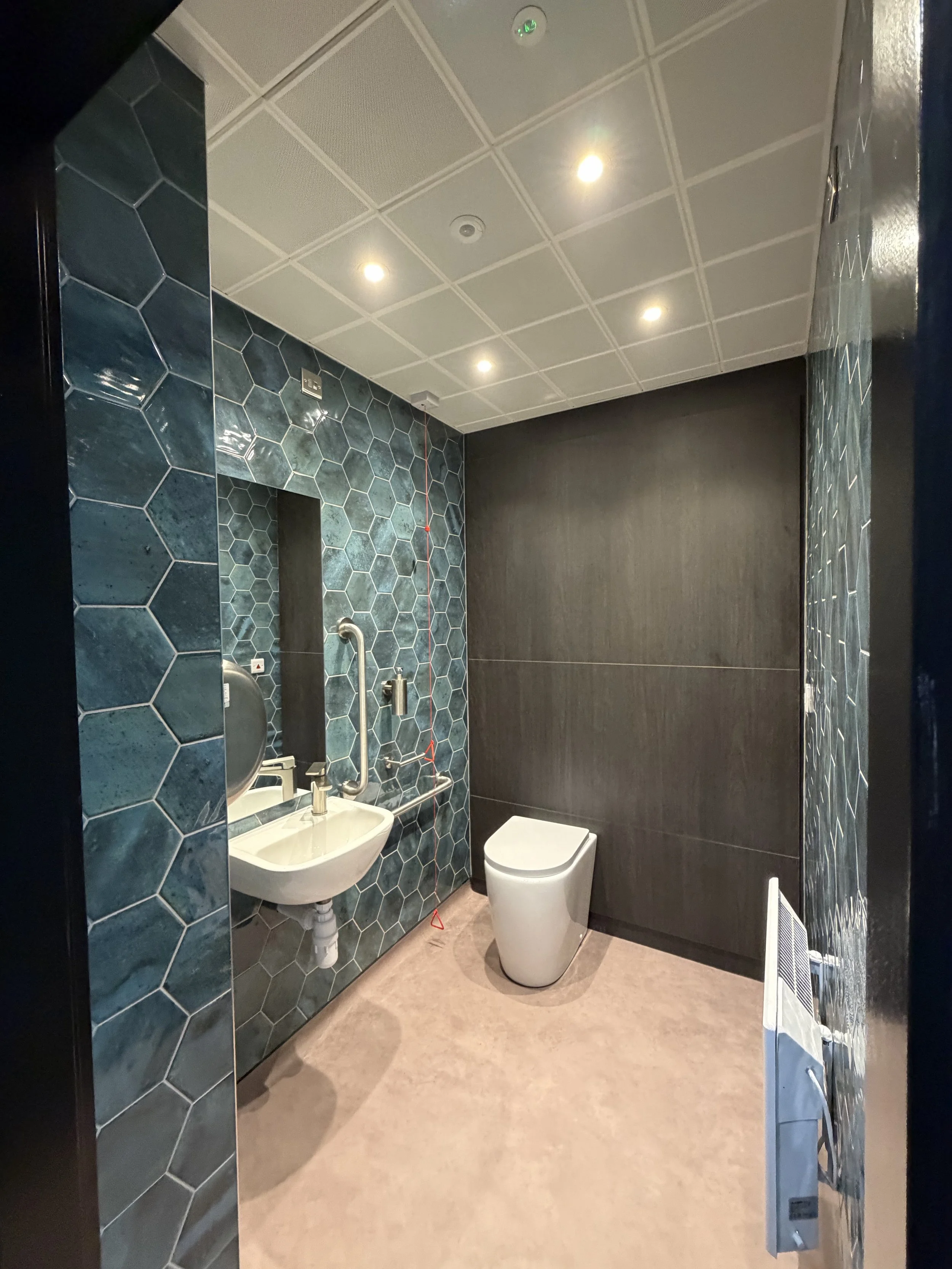 Accessible washroom at Portman Finance, Brackmills, with ceiling downlights, teal tiles, a basin, grab rails and toilet.