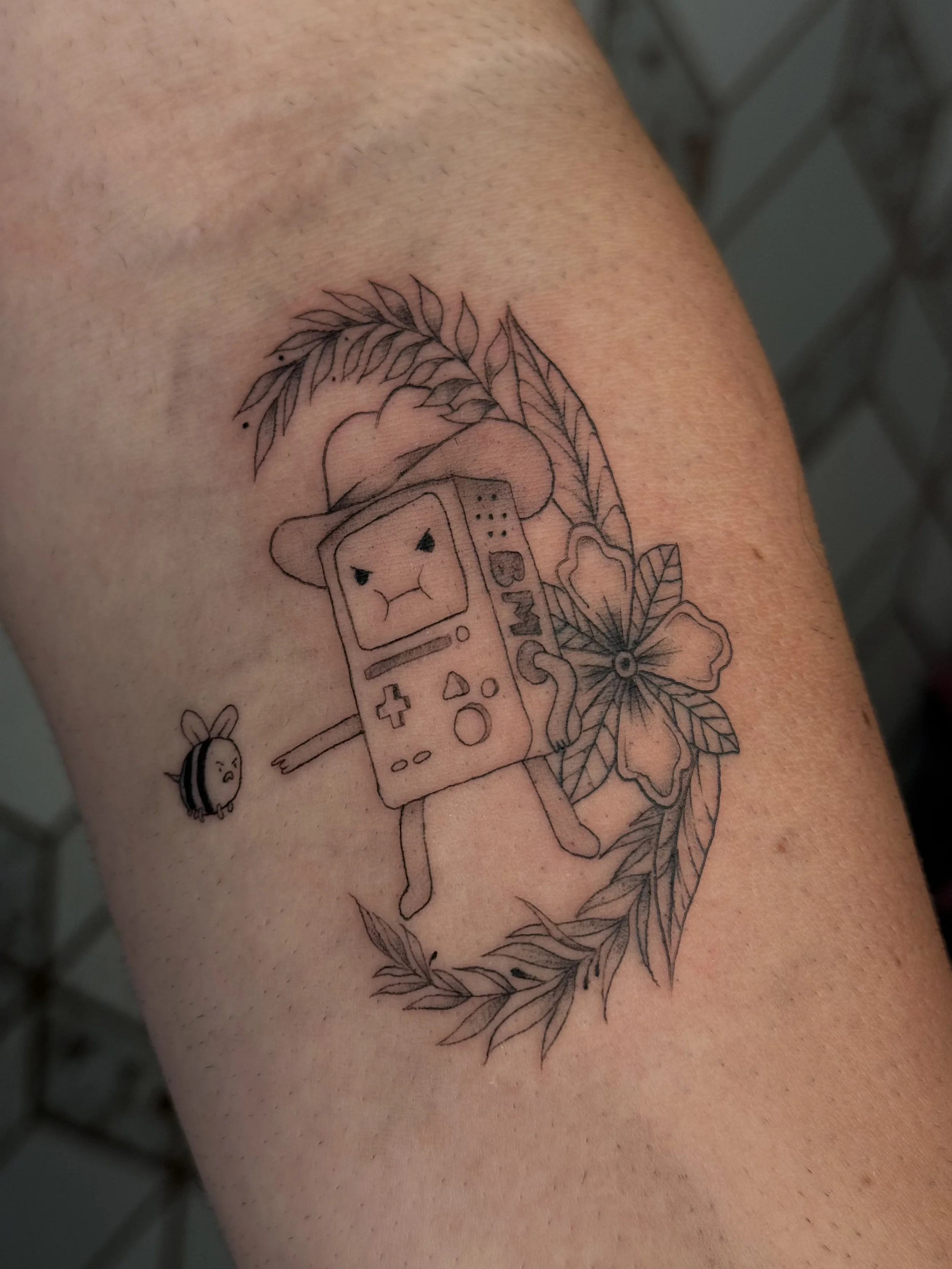 Fine line bmo character tattoo with american traditional inspired frame on arm in illustrative style
