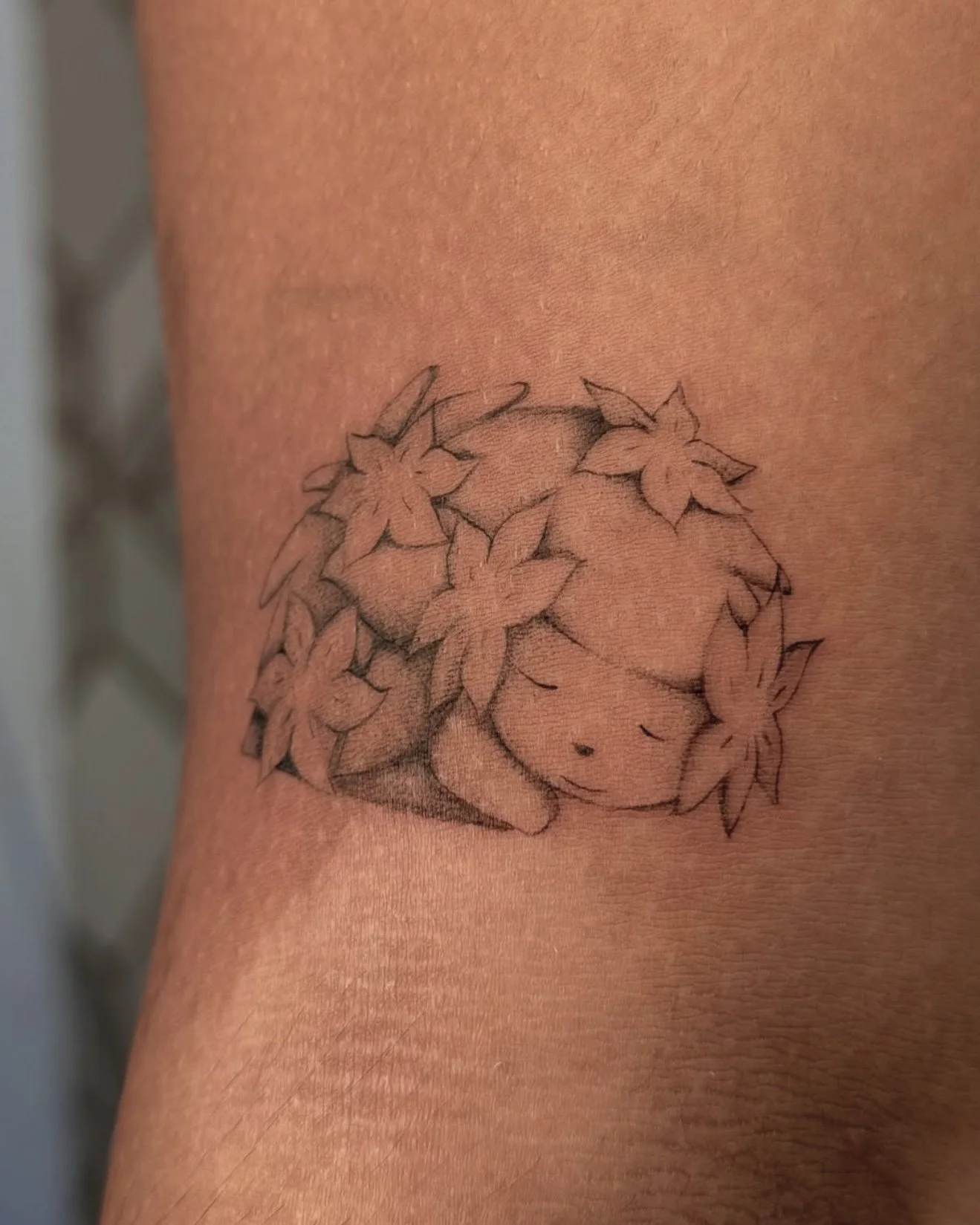 Tattoo of a cute pokemon inspired shaymin sleeping surrounded by cherry blossoms on skin.