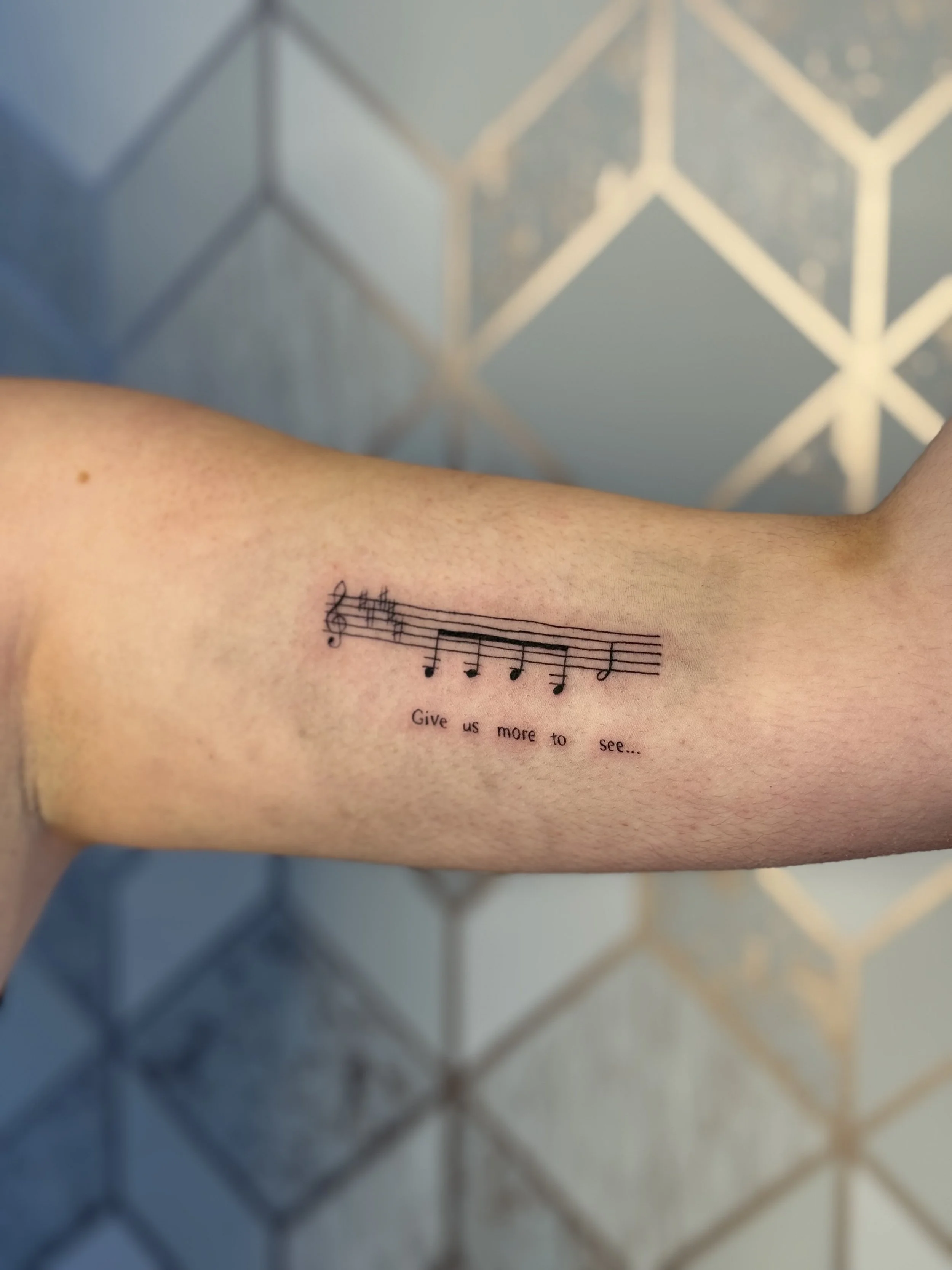 Fine line music staff tattoo with script text on inner forearm