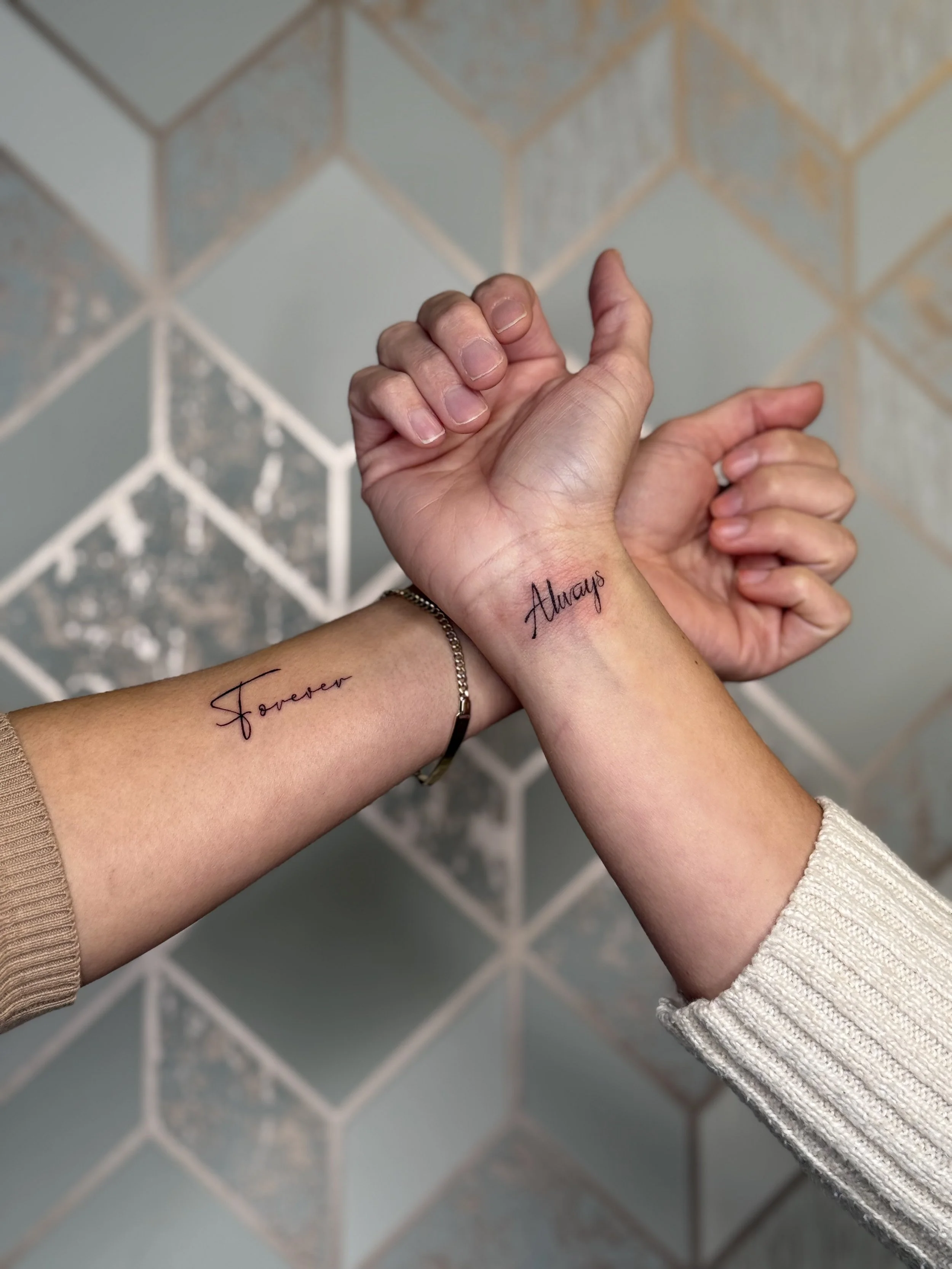 Fine line matching script tattoos on wrists in delicate handwritten lettering