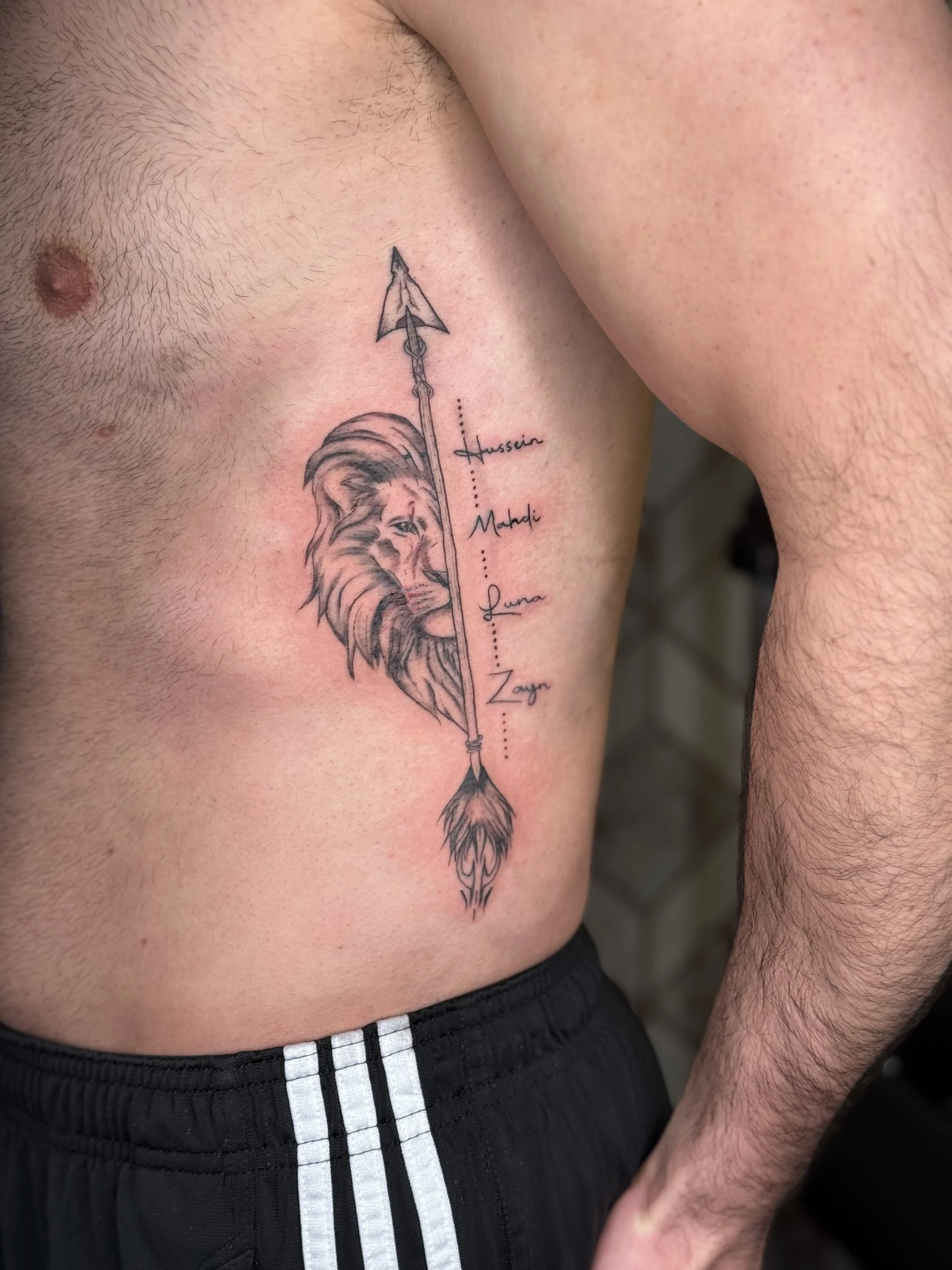 Fine line lion tattoo with vertical arrow and script details on ribs by a Dearborn fine line tattoo artist