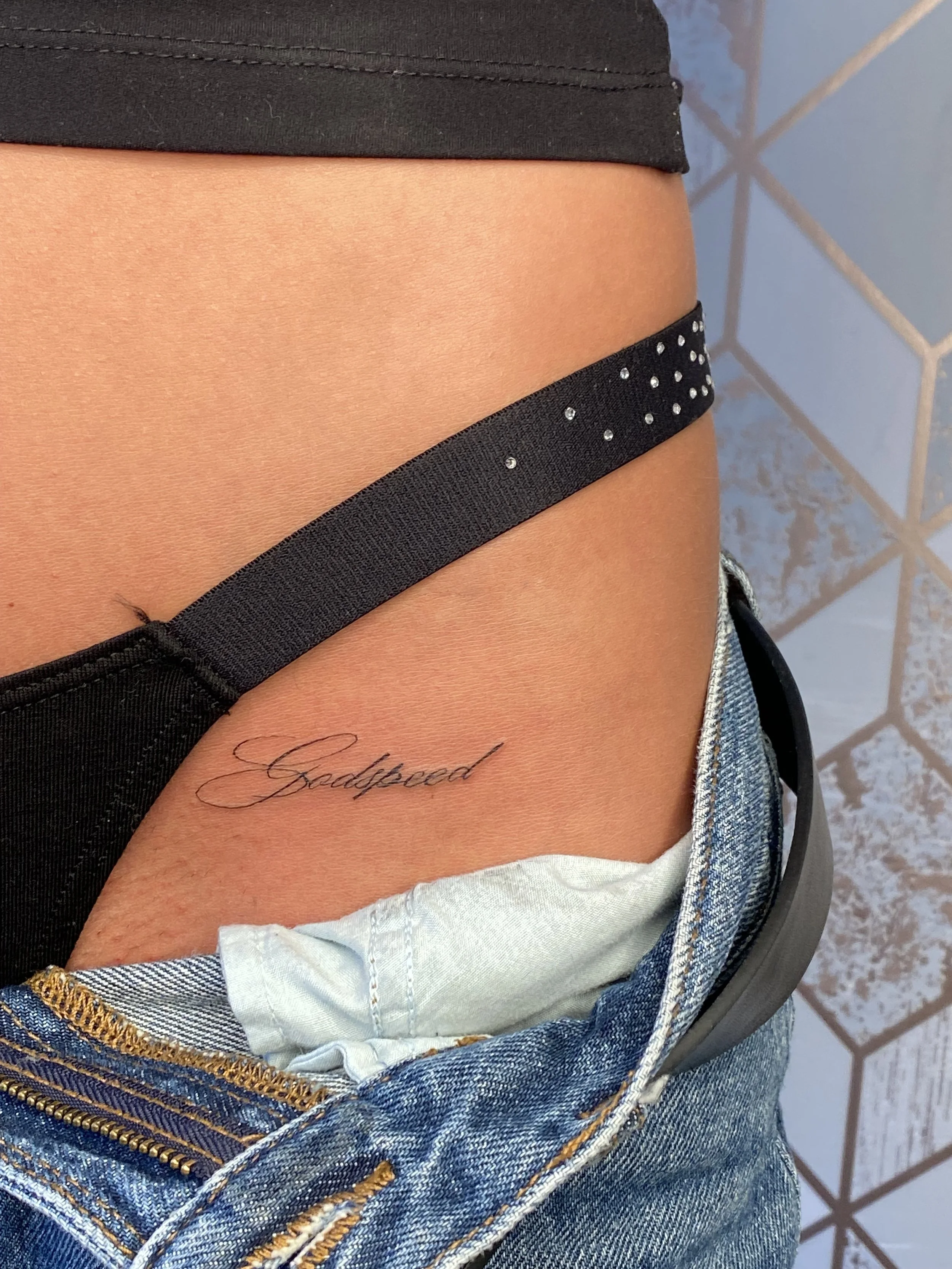 Fine line script tattoo placed along the hip in delicate lettering