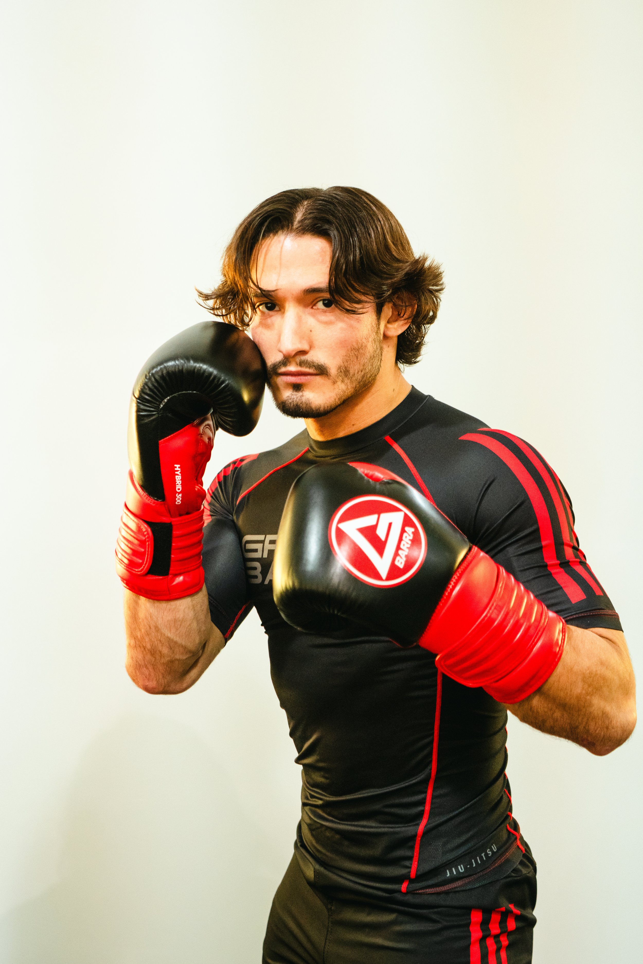 Coach Justin of Gracie Barra Bryan demonstrating a kickboxing stance, wearing black and red athletic gear and red boxing gloves.
