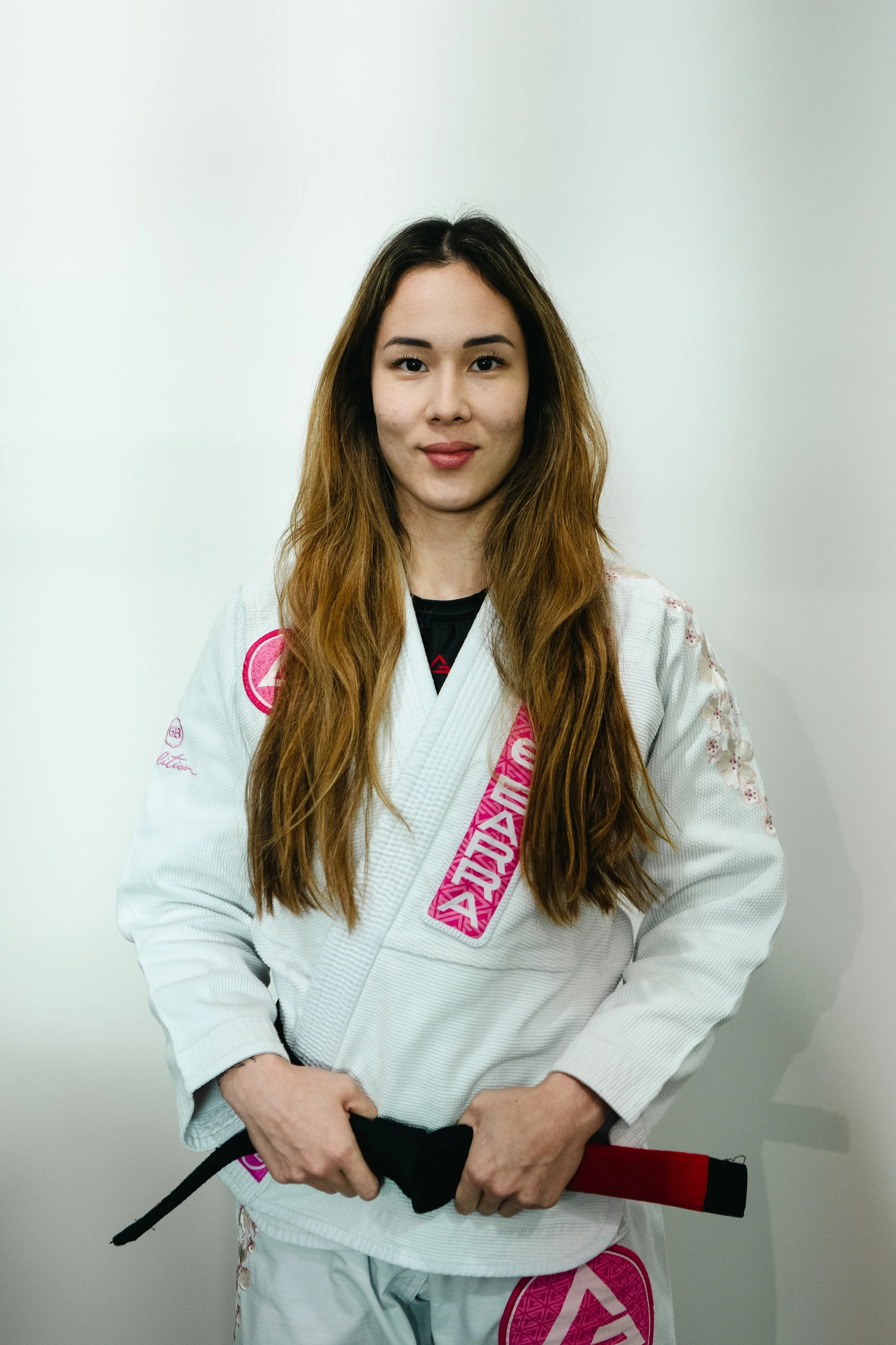 Professor Amanda of Gracie Barra Bryan wearing a white Brazilian Jiu-Jitsu gi holding black belt, standing against a white background.