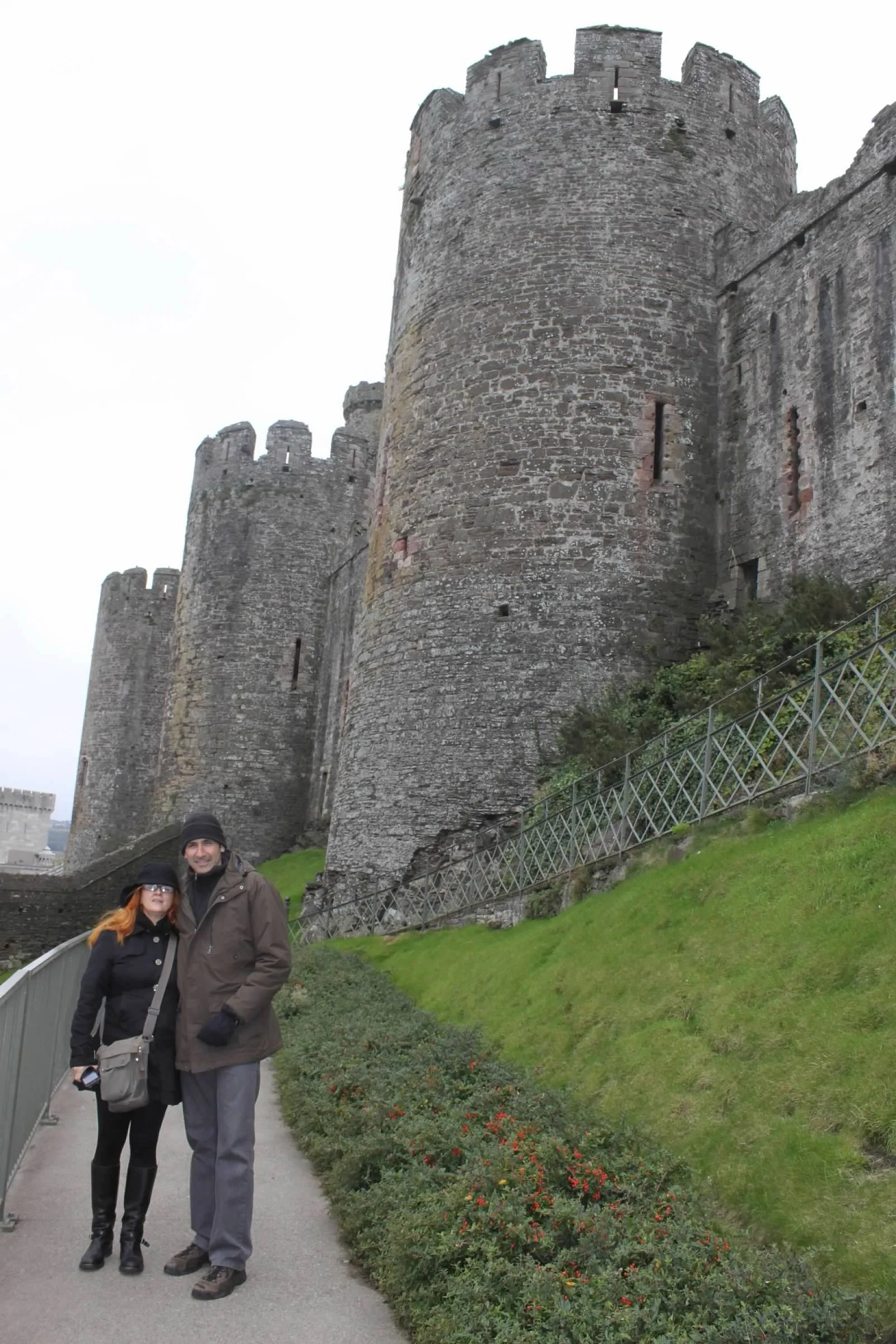 Two people standing in front of a large stone castle with tall towers and battlements.