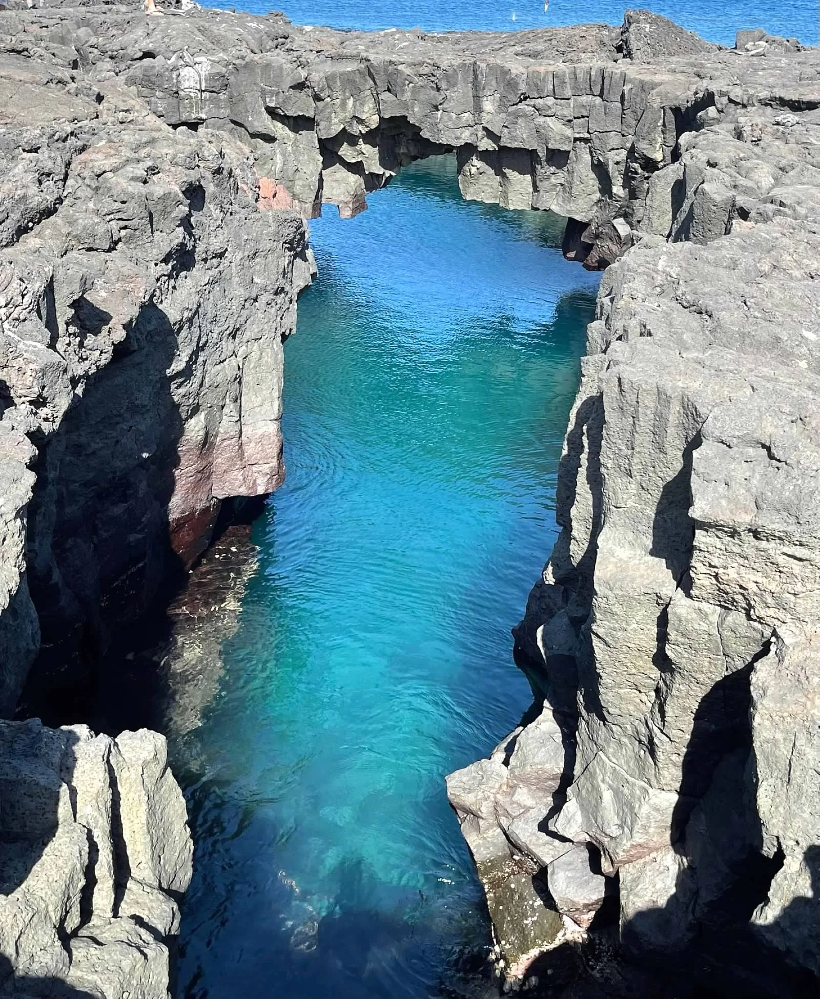 Rock formation creating a natural arch over turquoise water in a coastal landscape.
