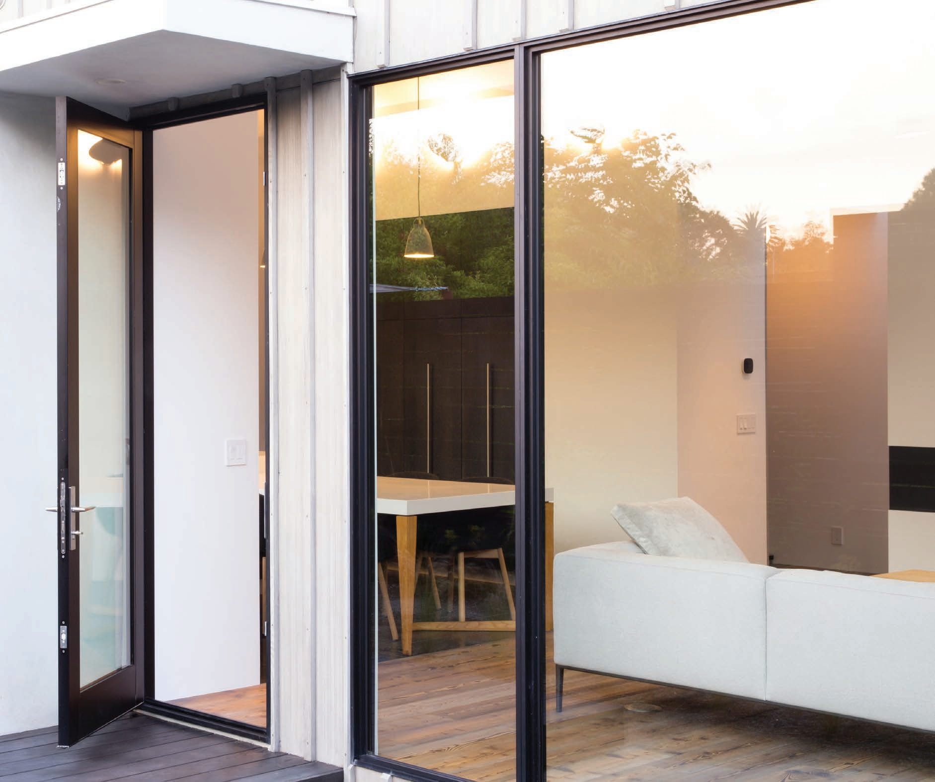 Modern living room with large glass sliding doors, white sofa, and wooden flooring; sunset view reflected on glass.