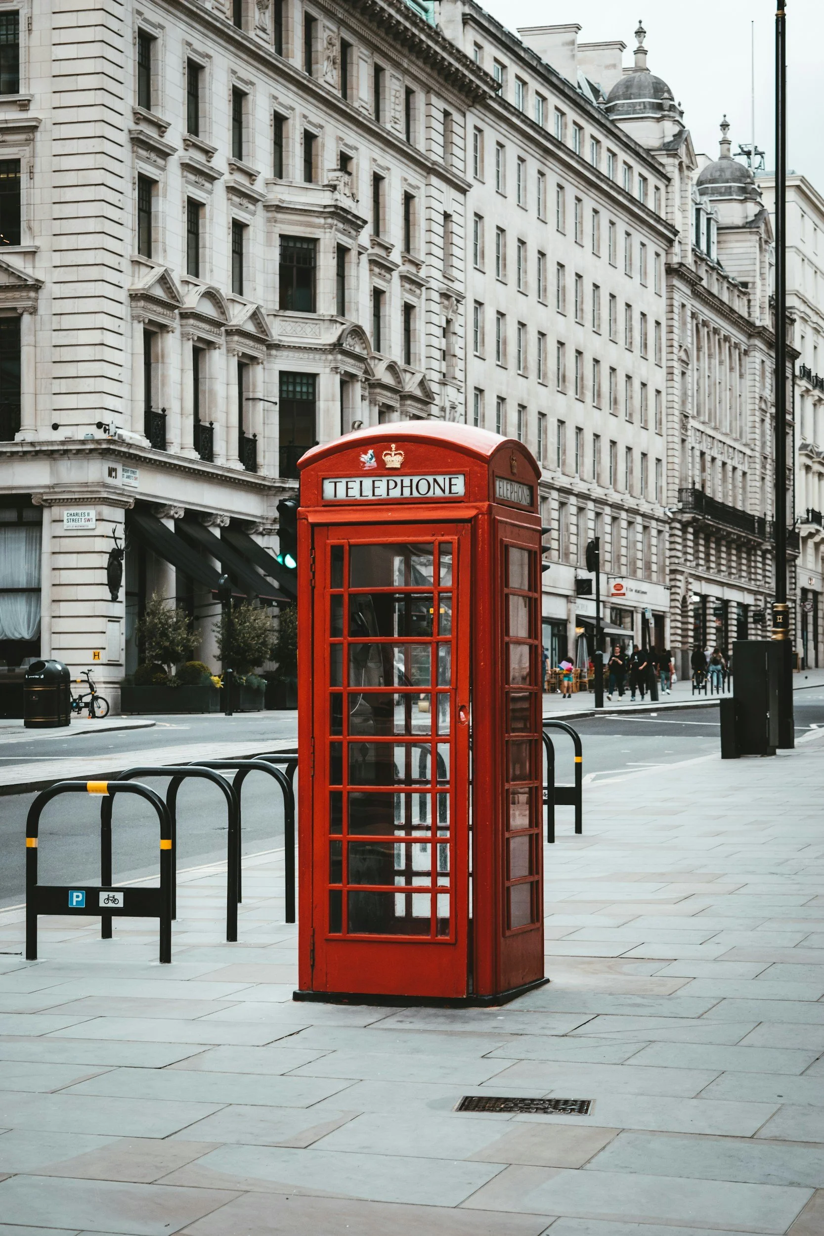 A classic red British telephone booth on a city sidewalk.