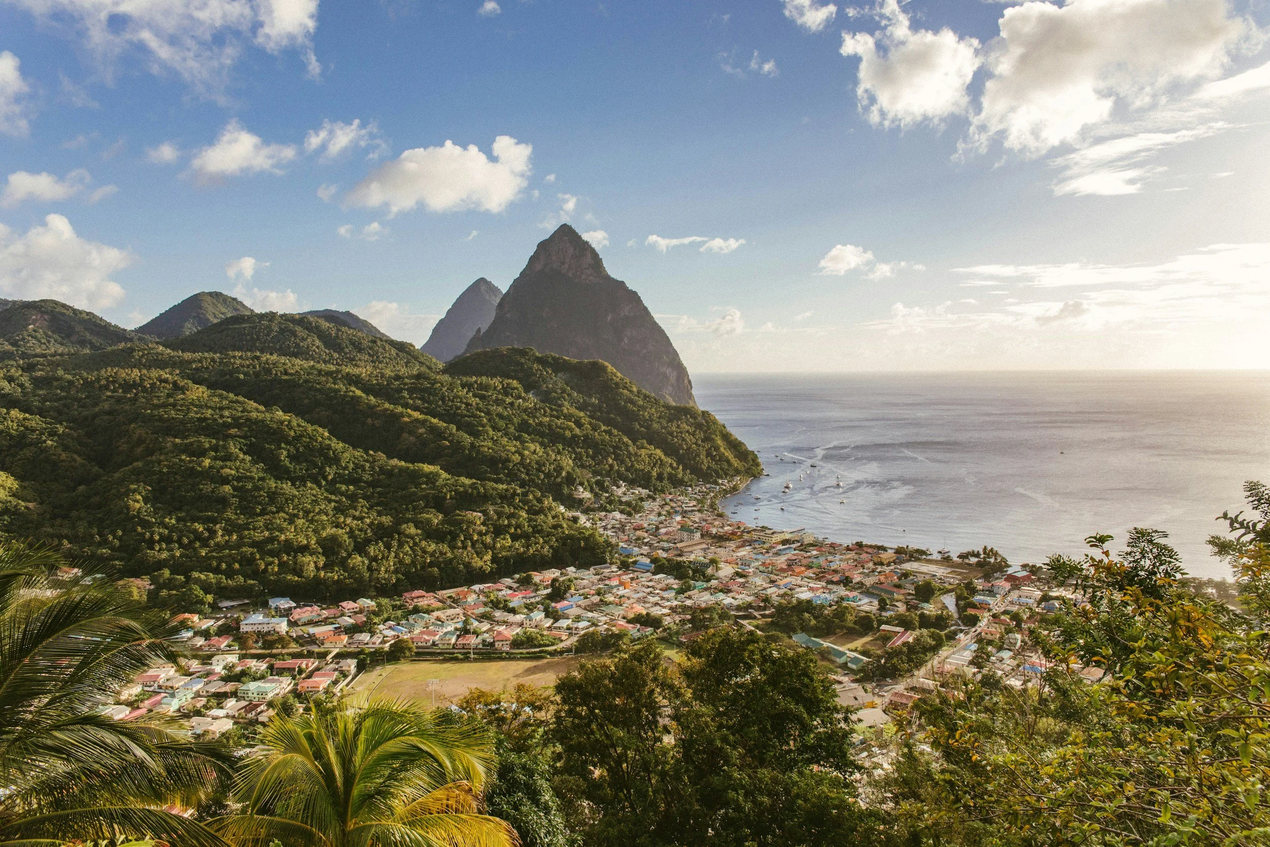 A coastal town nestled between lush green mountains and the ocean, with boats on the water and houses along the shoreline.