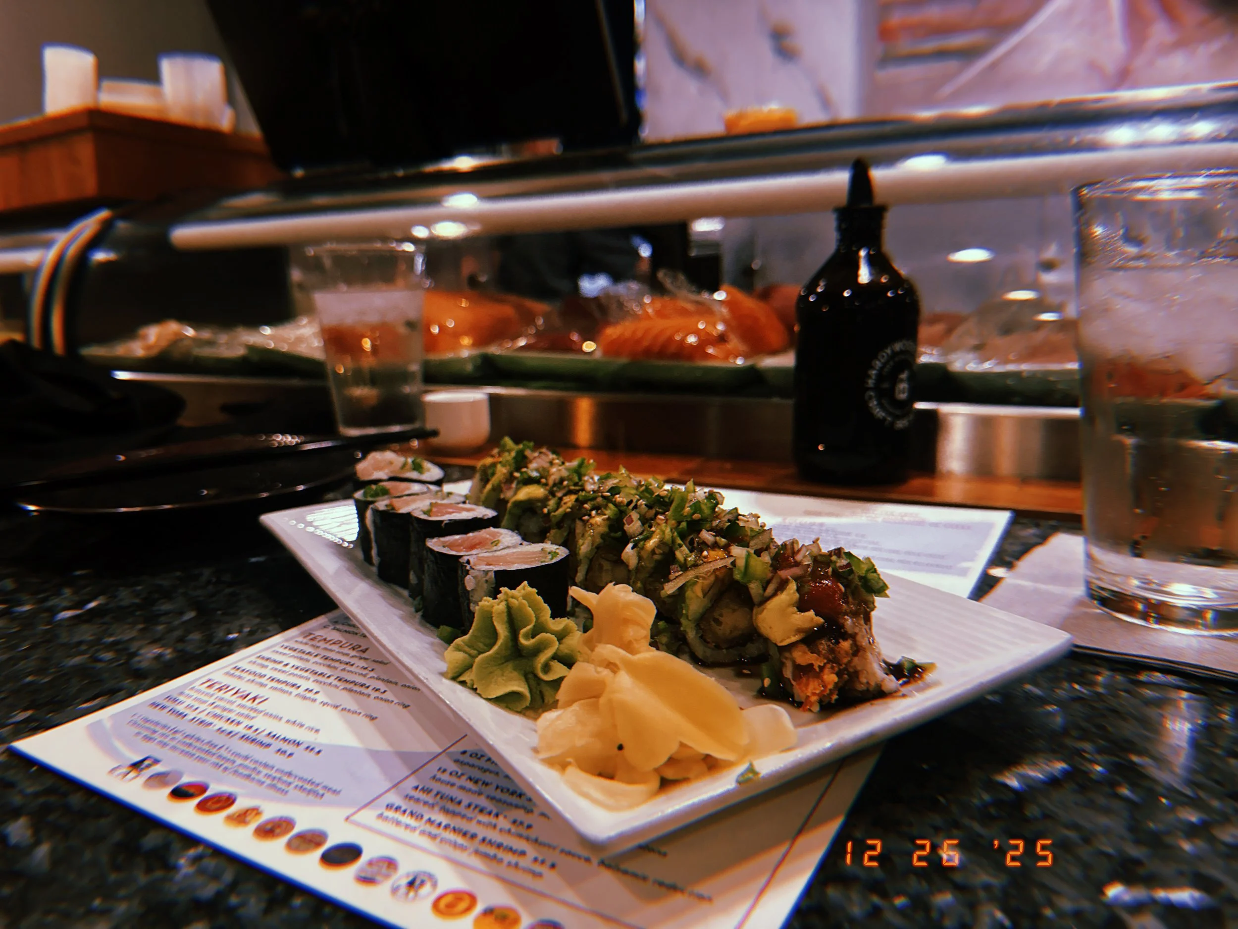 Close-up of a plate of sushi with wasabi, ginger, and green onions on a restaurant counter.